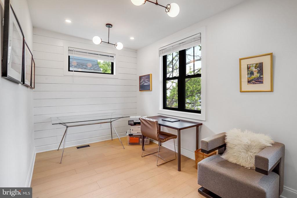 Home office with a desk beside a large black-framed window and a gray armchair.