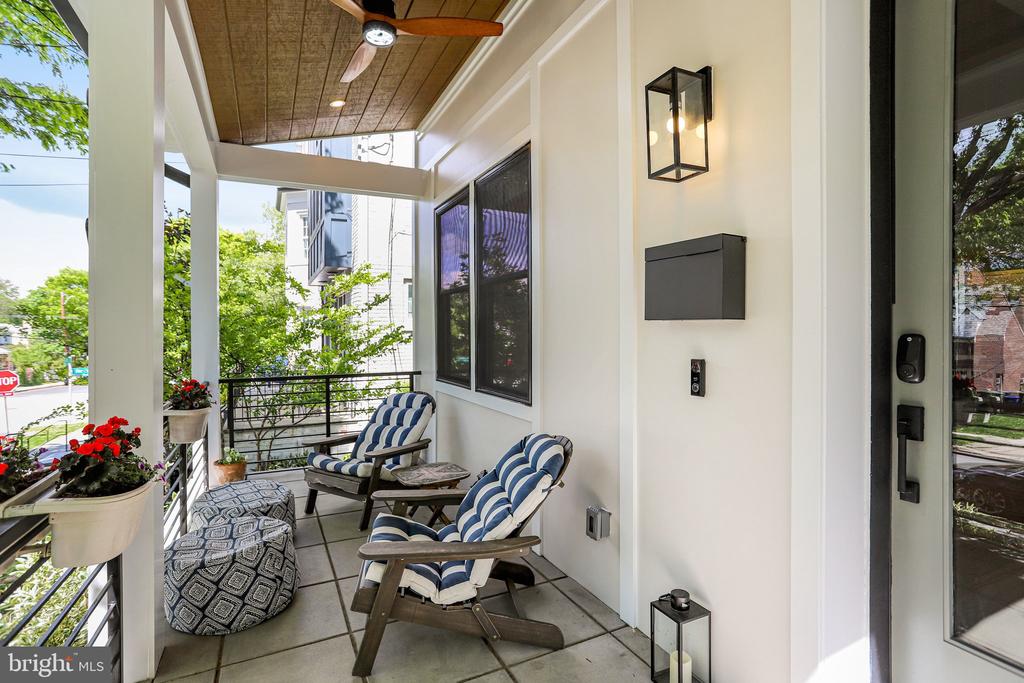 Covered front porch with blue-and-white cushioned chairs, tiled floor, ceiling fan, and flower planters.