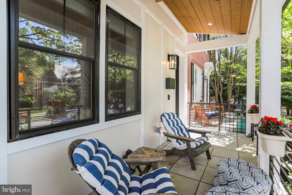 Covered front porch with blue-and-white cushioned chairs, wood ceiling, and potted flowers.