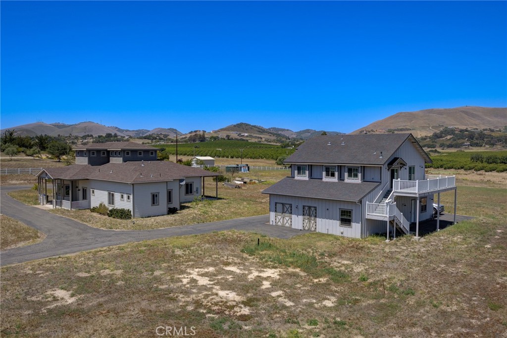 Rural property with two gray buildings, a paved drive, vineyard rows, and rolling hills.