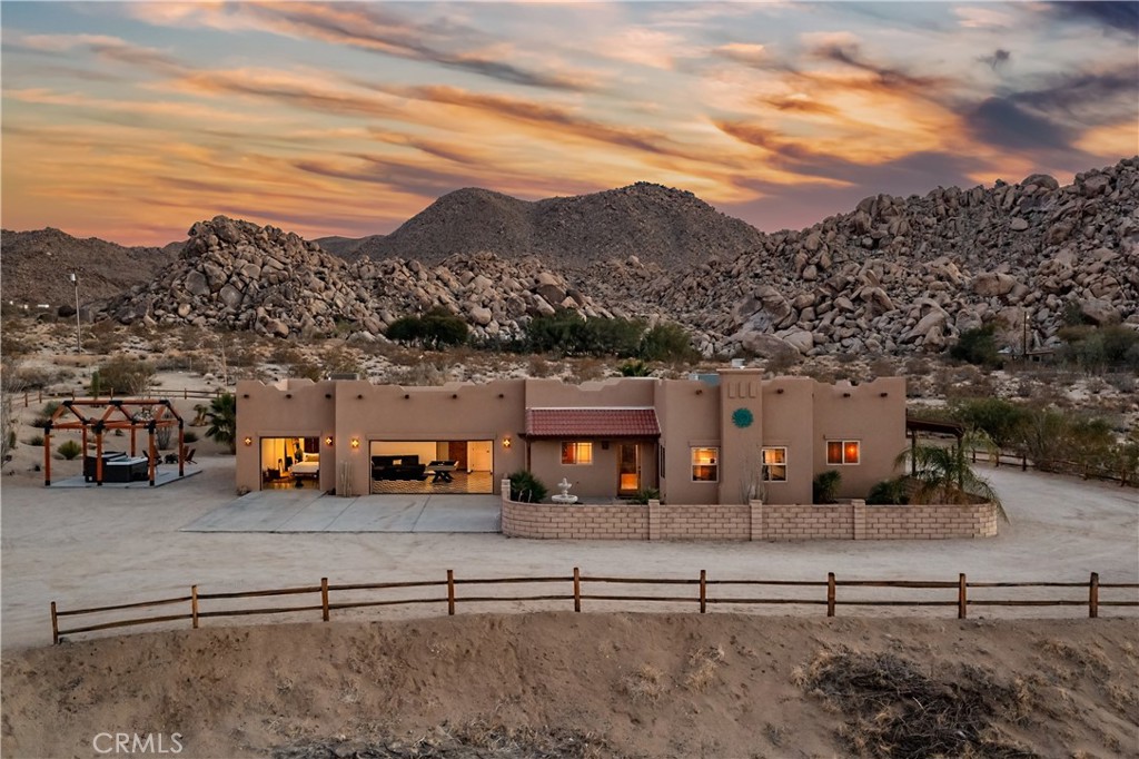Desert home beneath rocky hills at sunset, with a broad courtyard and low adobe-style exterior.