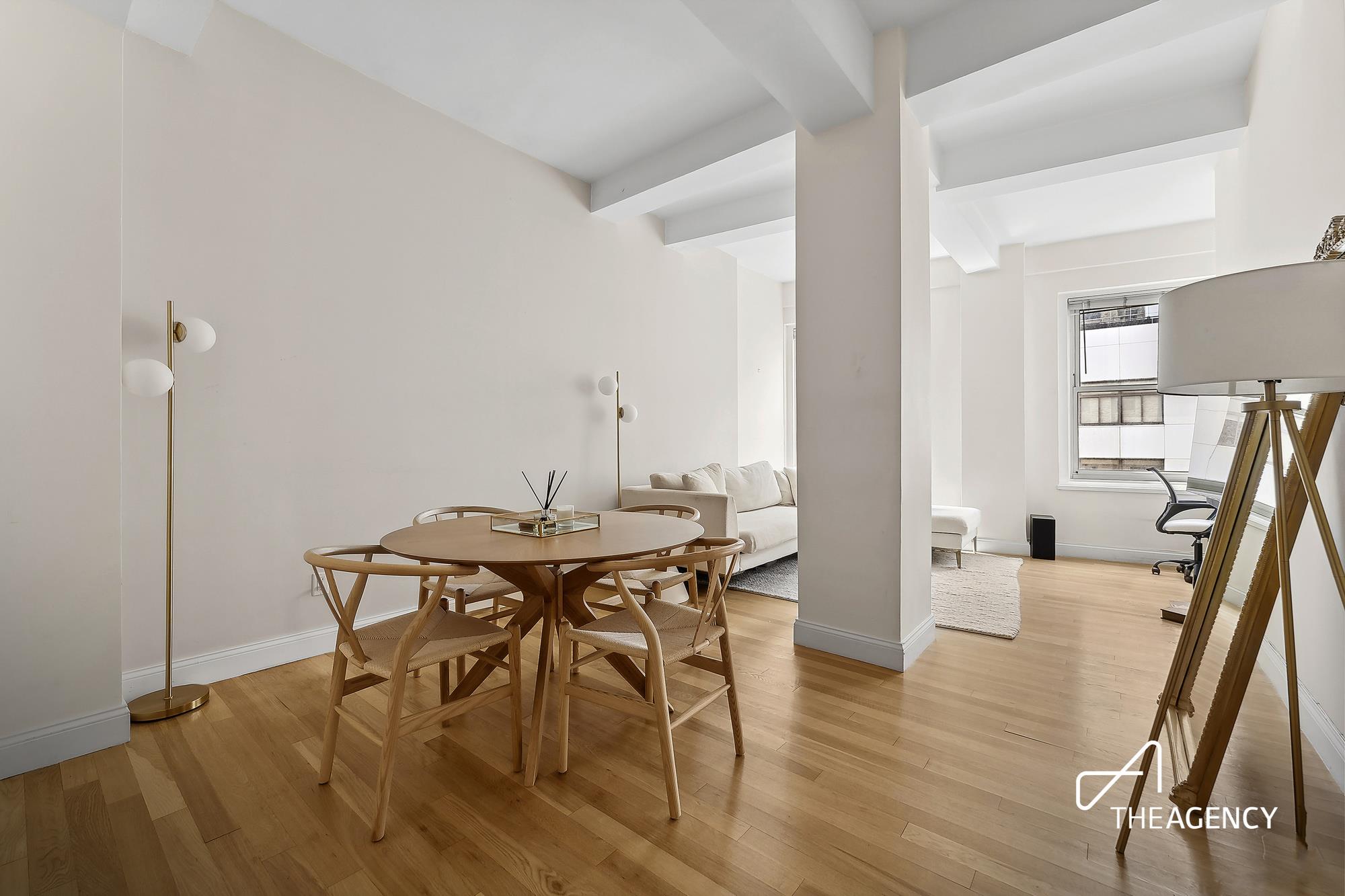 Dining area with a round wooden table beside a pale sofa in a bright open-plan interior.