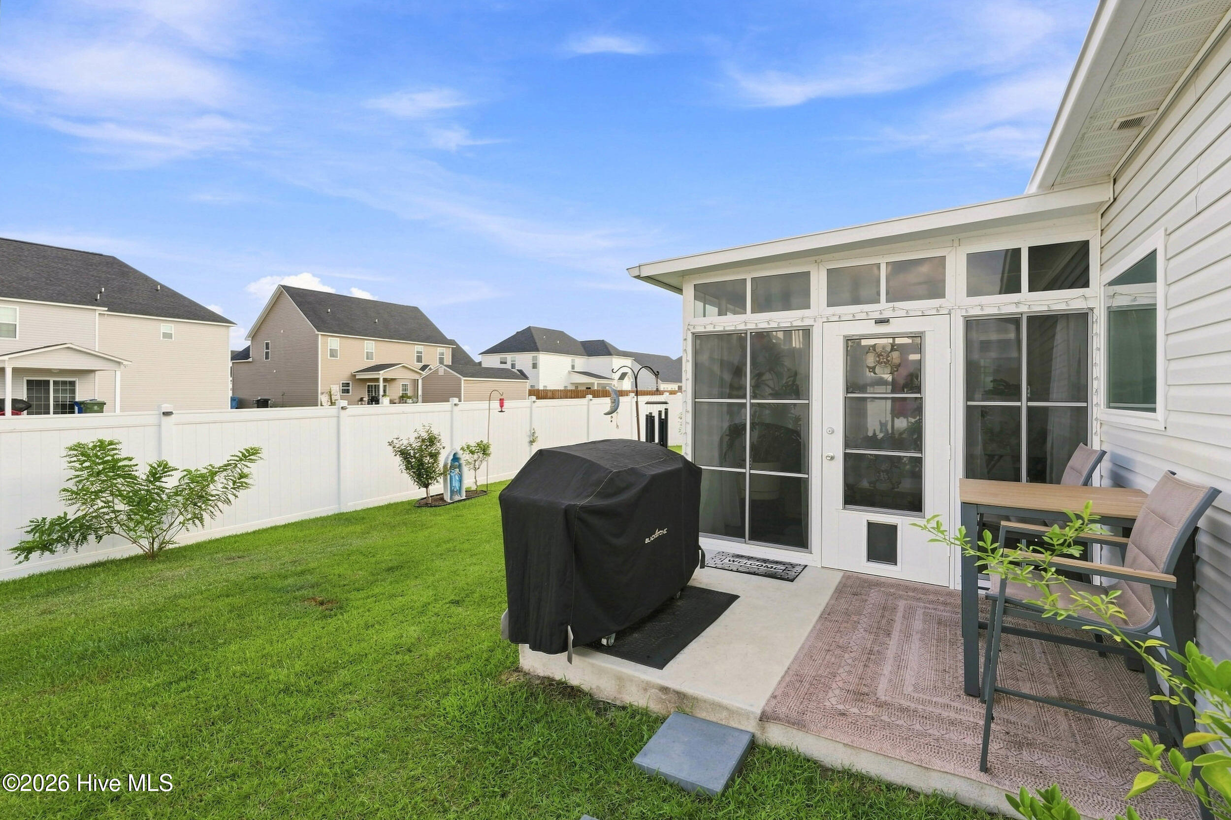 Backyard patio with a covered grill, outdoor dining set, fenced lawn, and glass-enclosed sunroom.