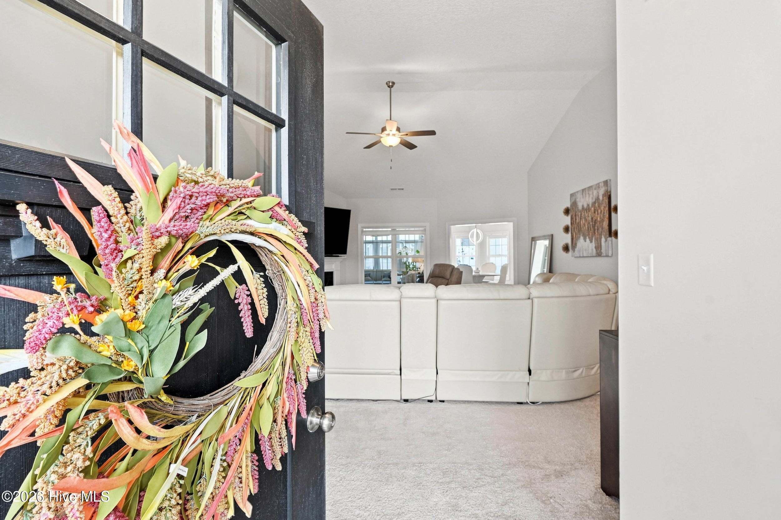Bright living room seen through an open black door with a colorful floral wreath and white sectional sofa.