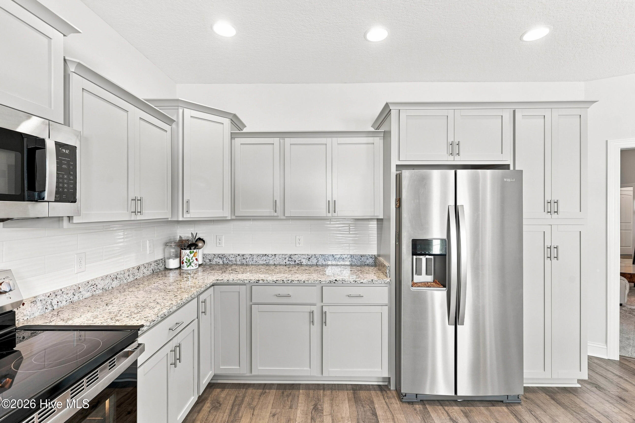 Kitchen with white shaker cabinets, speckled stone counters, and stainless steel appliances.