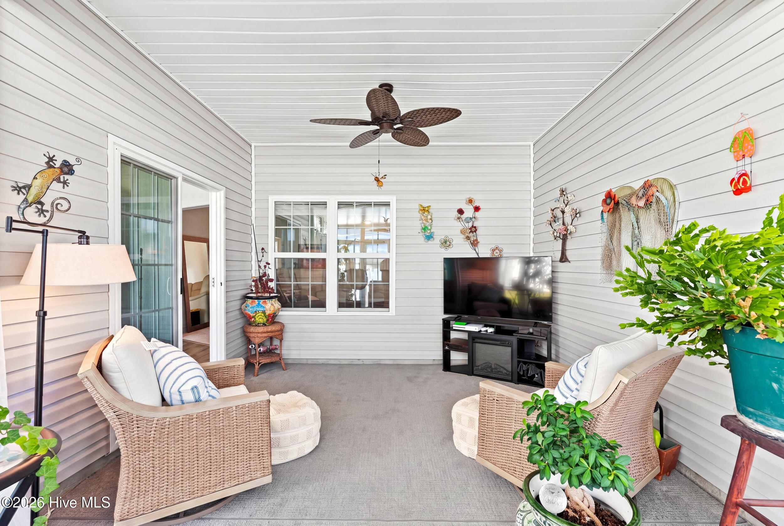 Covered porch with wicker seating, a ceiling fan, and a television.
