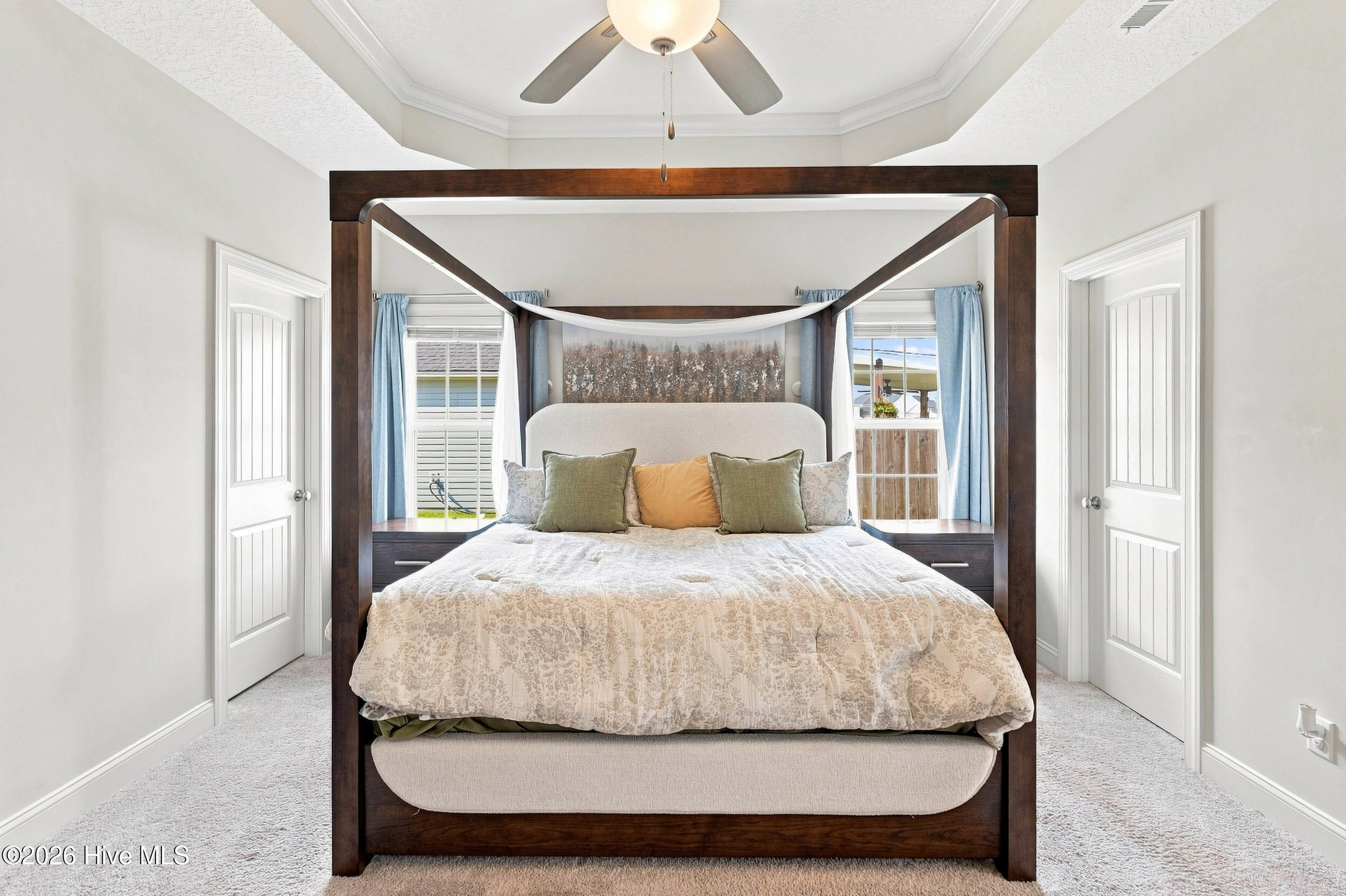 Staged bedroom with a dark wood four-poster bed, patterned white bedding, and blue curtains.