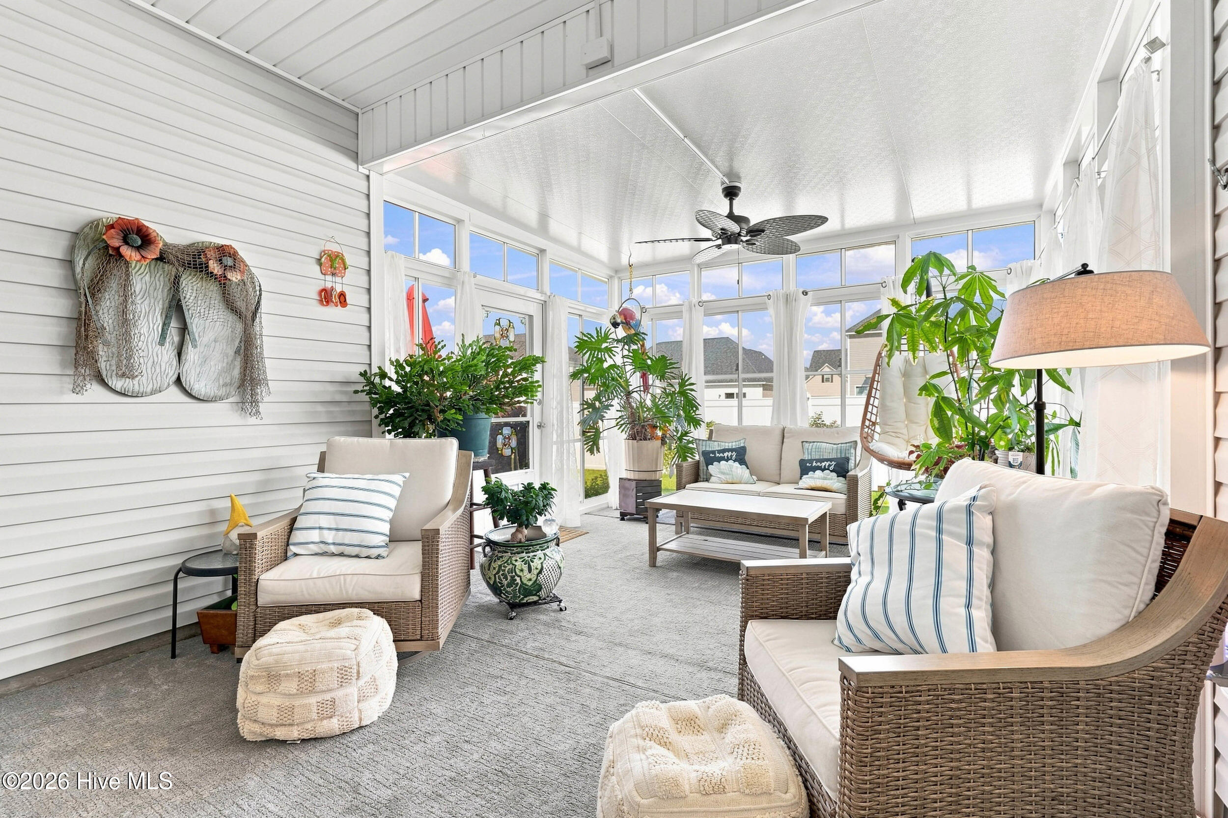 Bright sunroom with wicker seating, large windows, potted plants, and a ceiling fan.