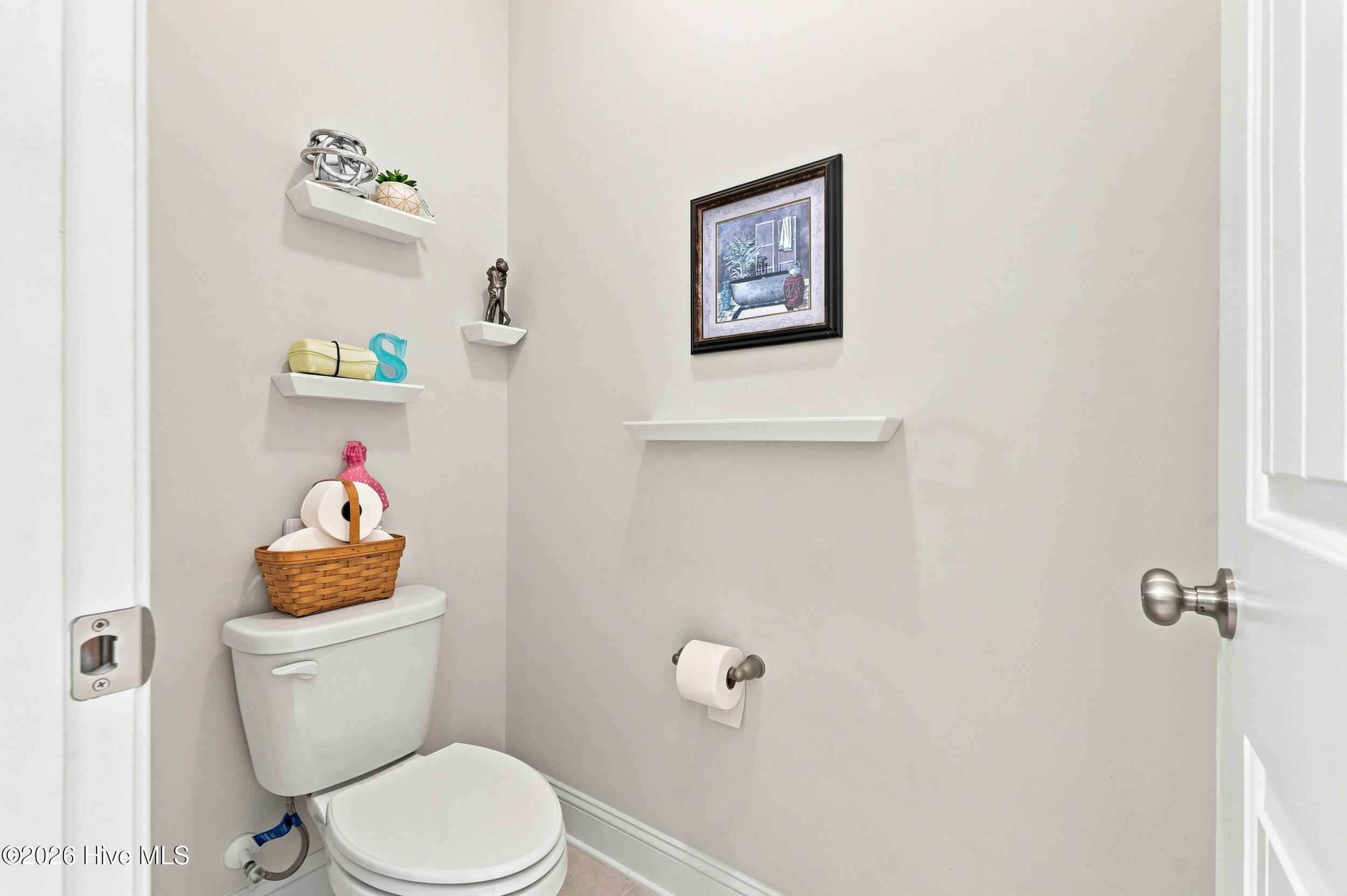 Bathroom with a white toilet, decorative floating shelves, and framed artwork.