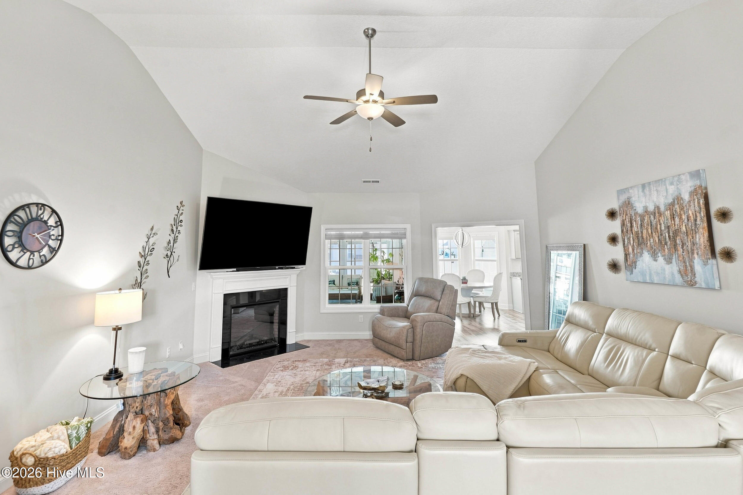 Furnished living room with a vaulted ceiling, white sectional, fireplace, and mounted television.