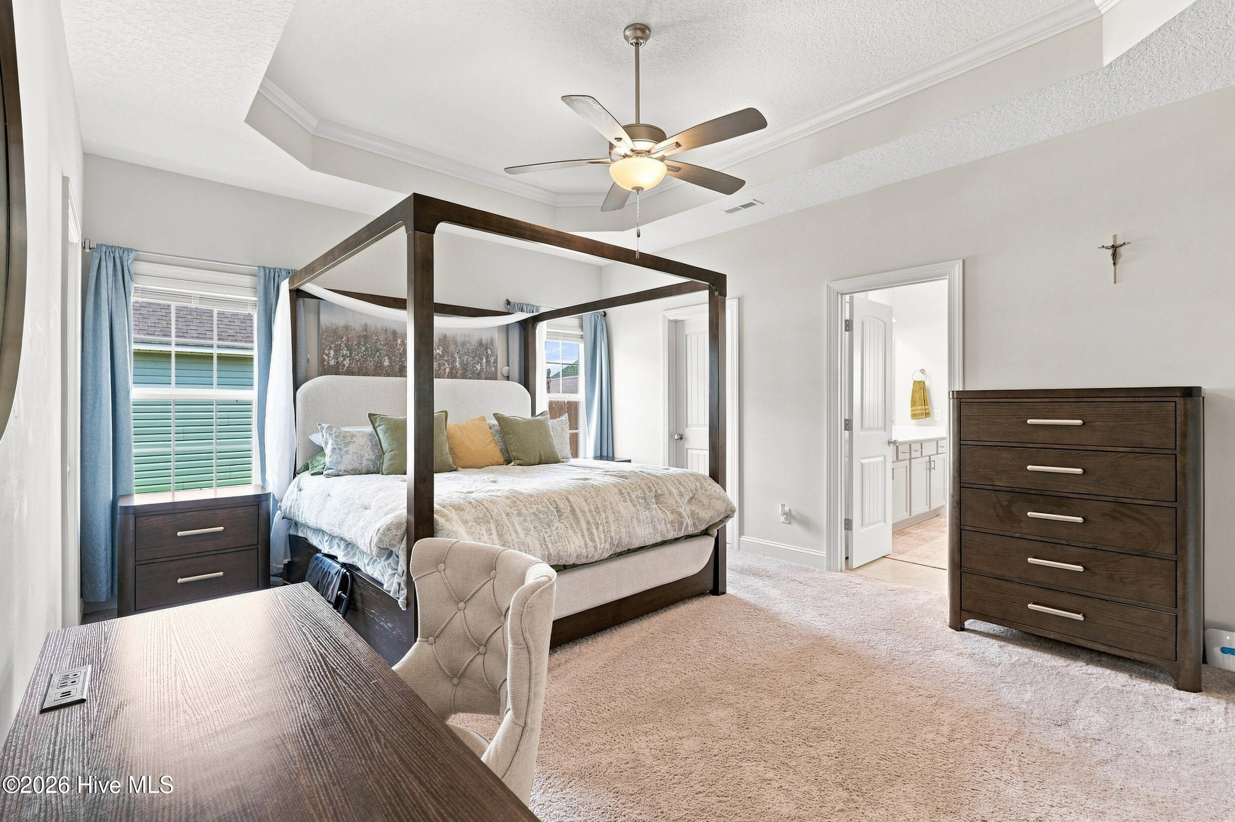 Furnished bedroom with a dark four-poster bed, blue curtains, tray ceiling and adjoining bathroom.