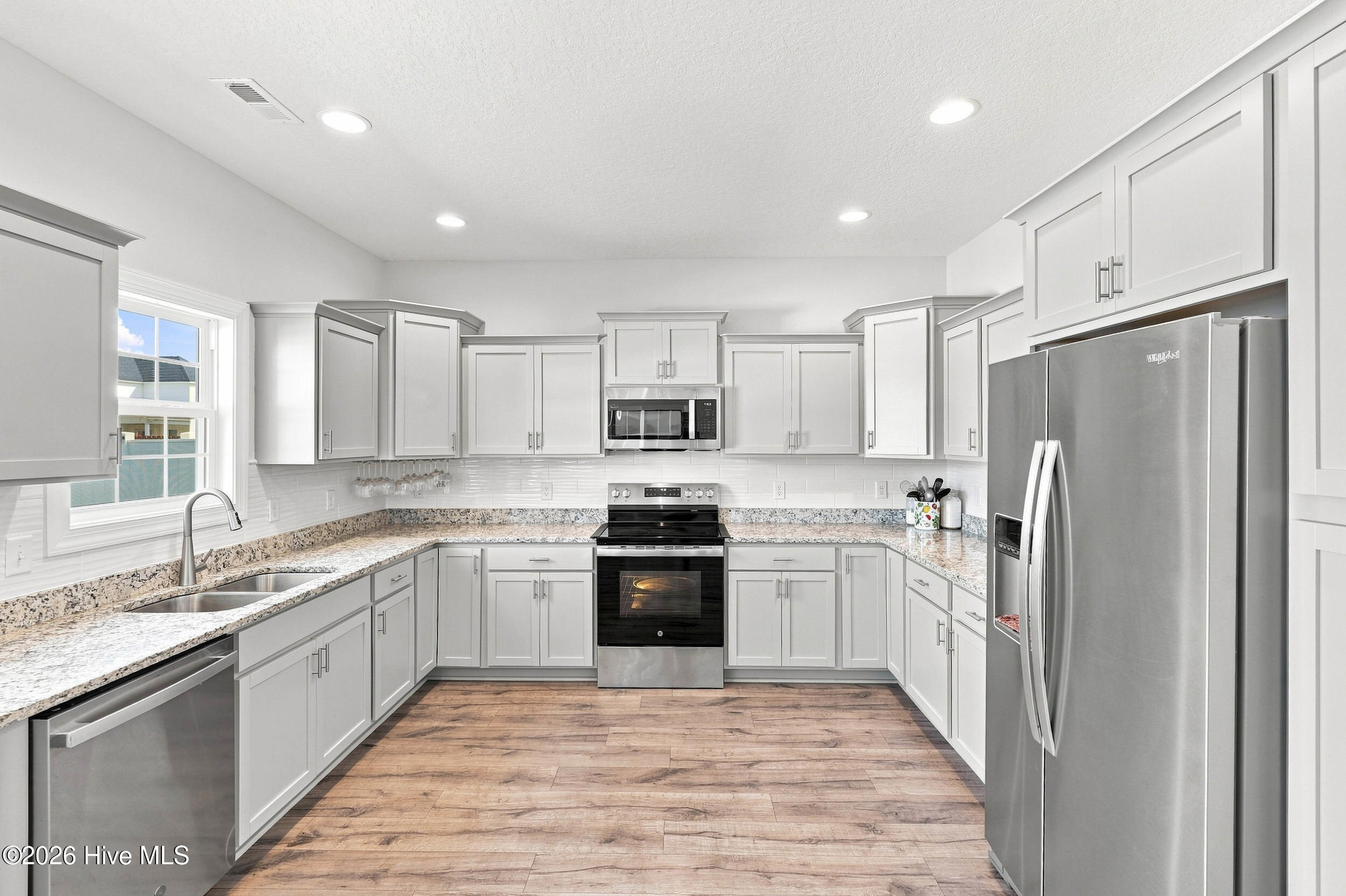 Bright kitchen with white cabinets, granite counters, stainless steel appliances, and wood-look floors.