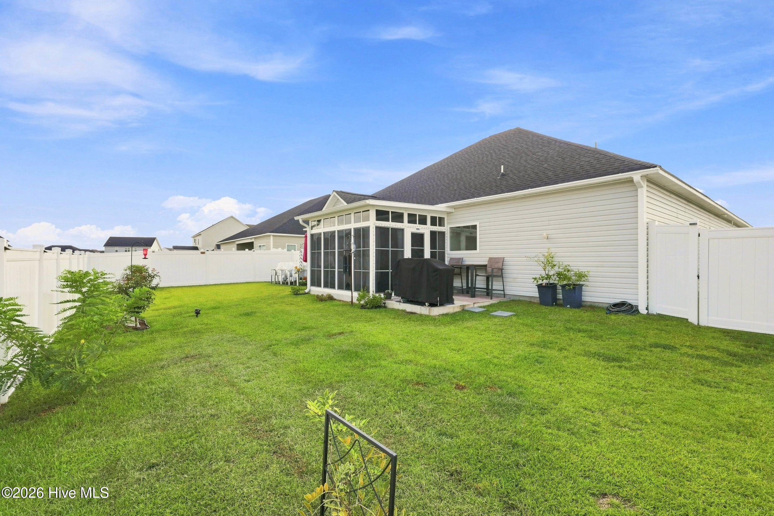 Fenced backyard with a broad lawn, screened sunroom, and patio seating.
