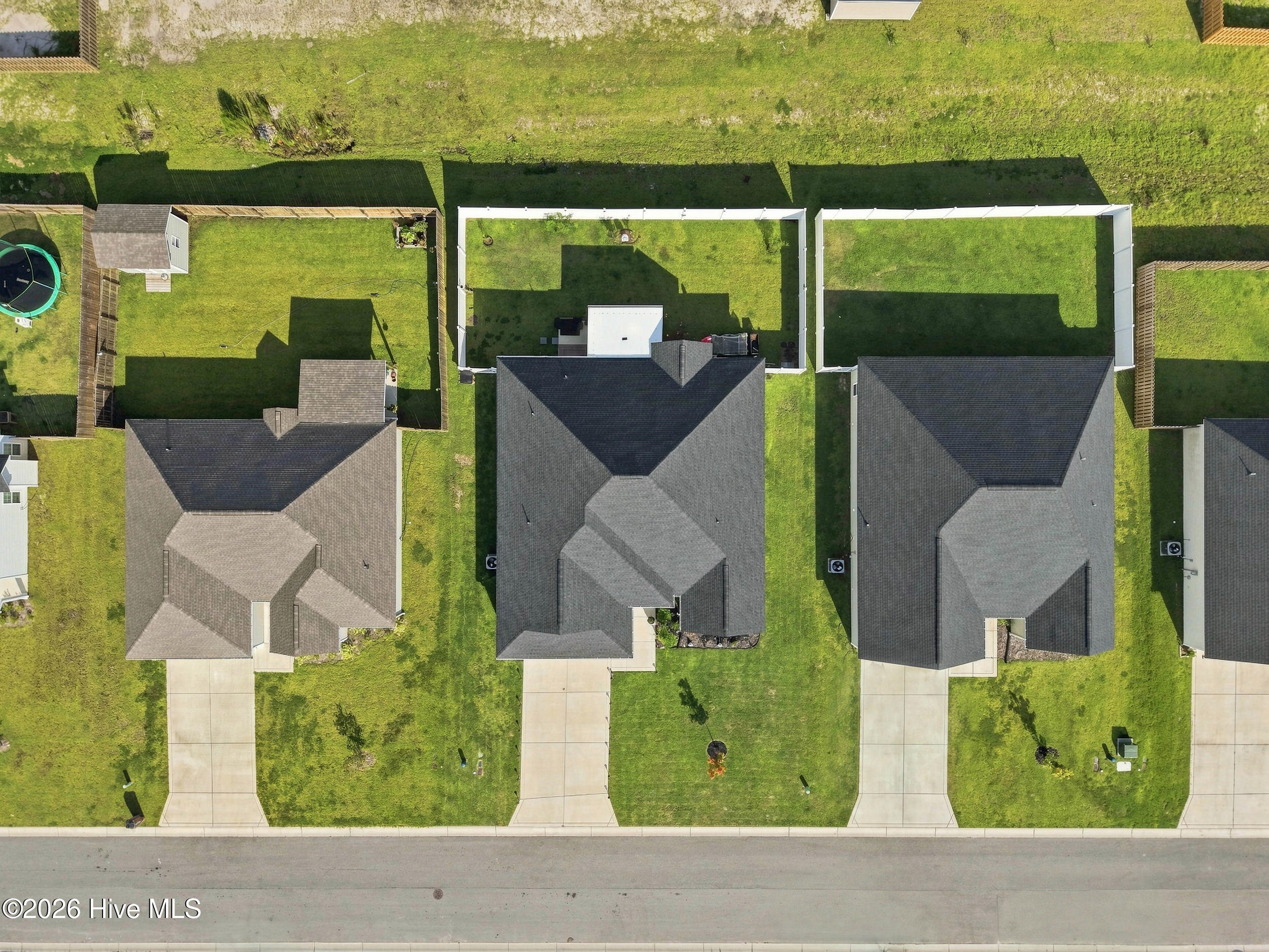 Aerial view of neighboring homes and fenced backyards, with the center house’s dark roof visible.