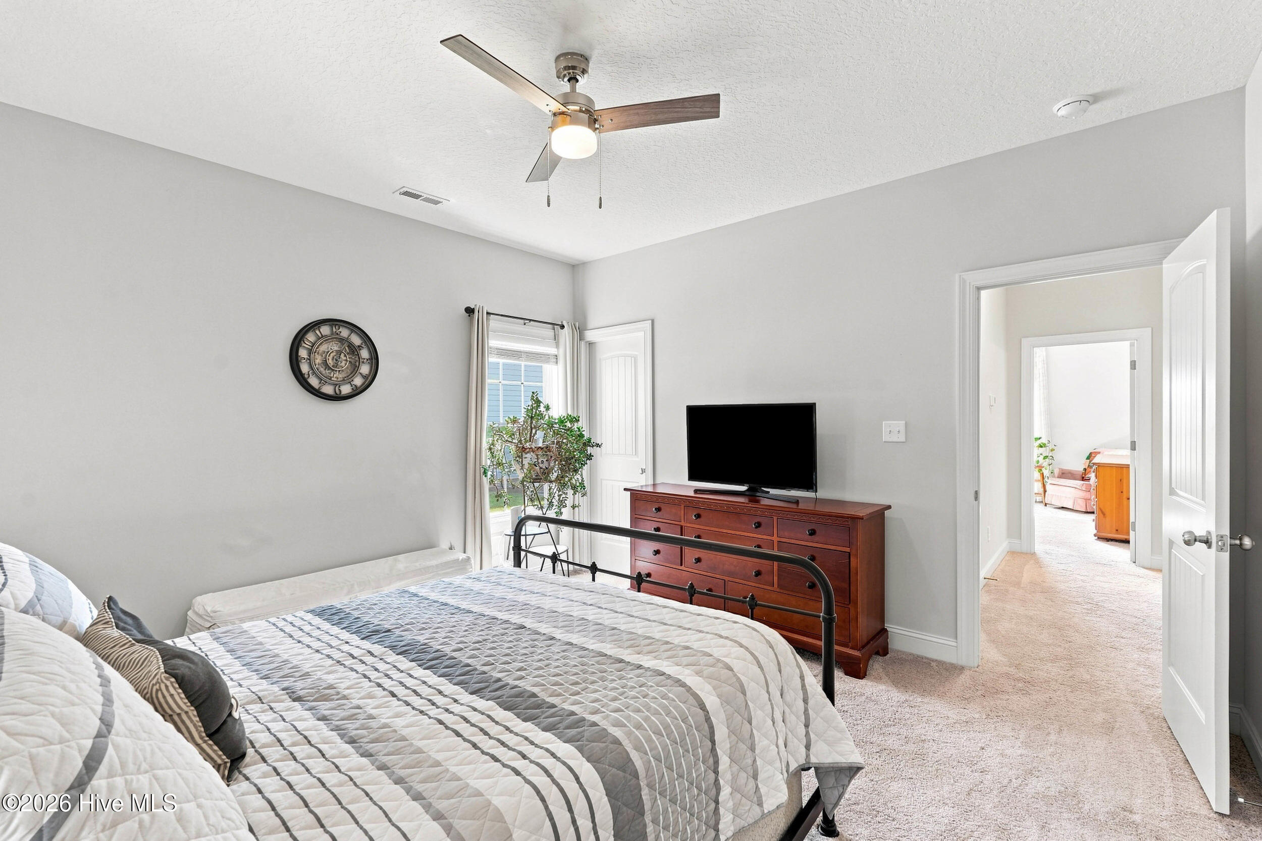Bedroom with a gray-and-white quilted bed, wooden dresser, television, and open doorway.
