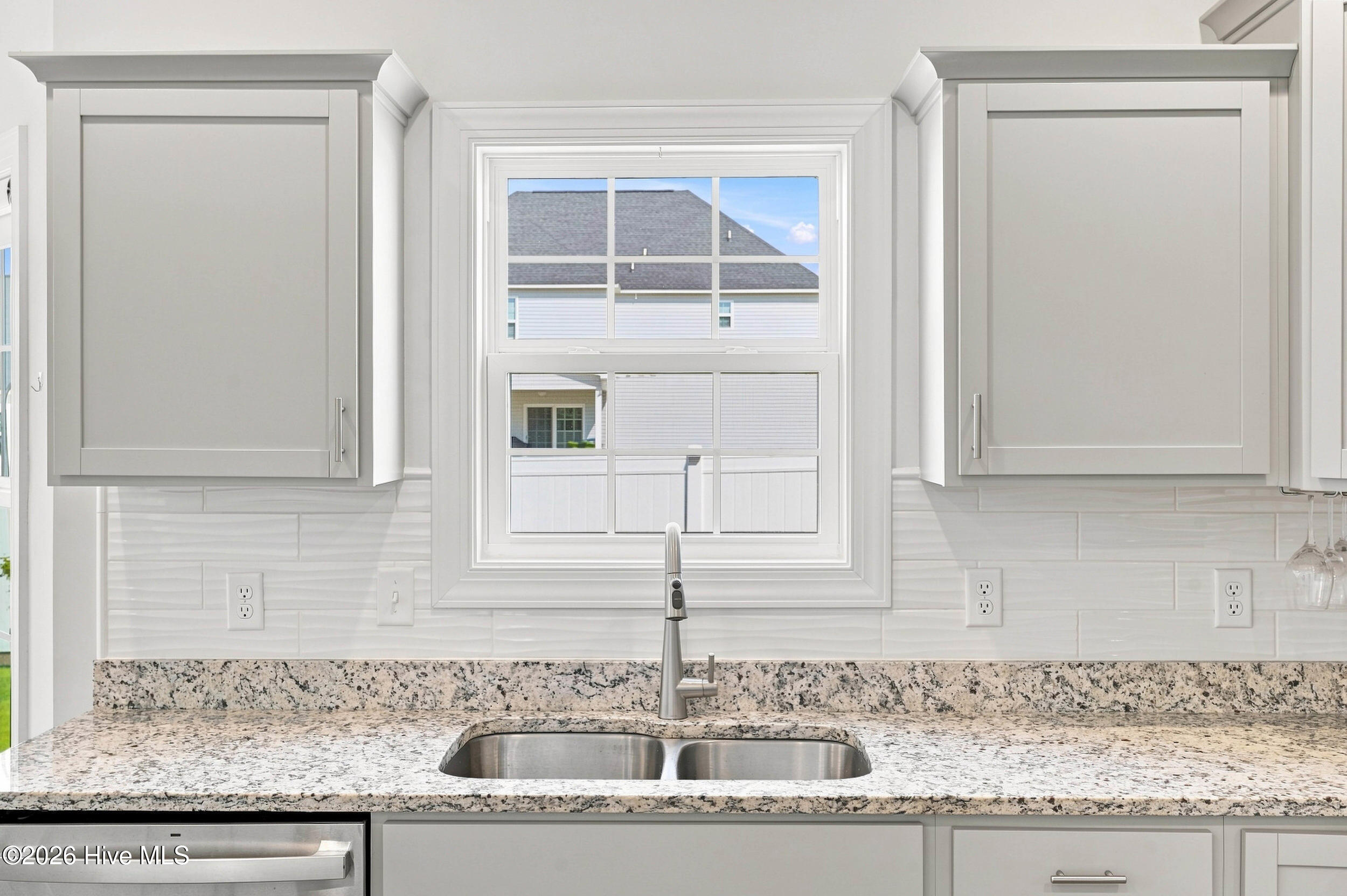 Kitchen sink beneath a window, with white cabinets and a speckled granite countertop.