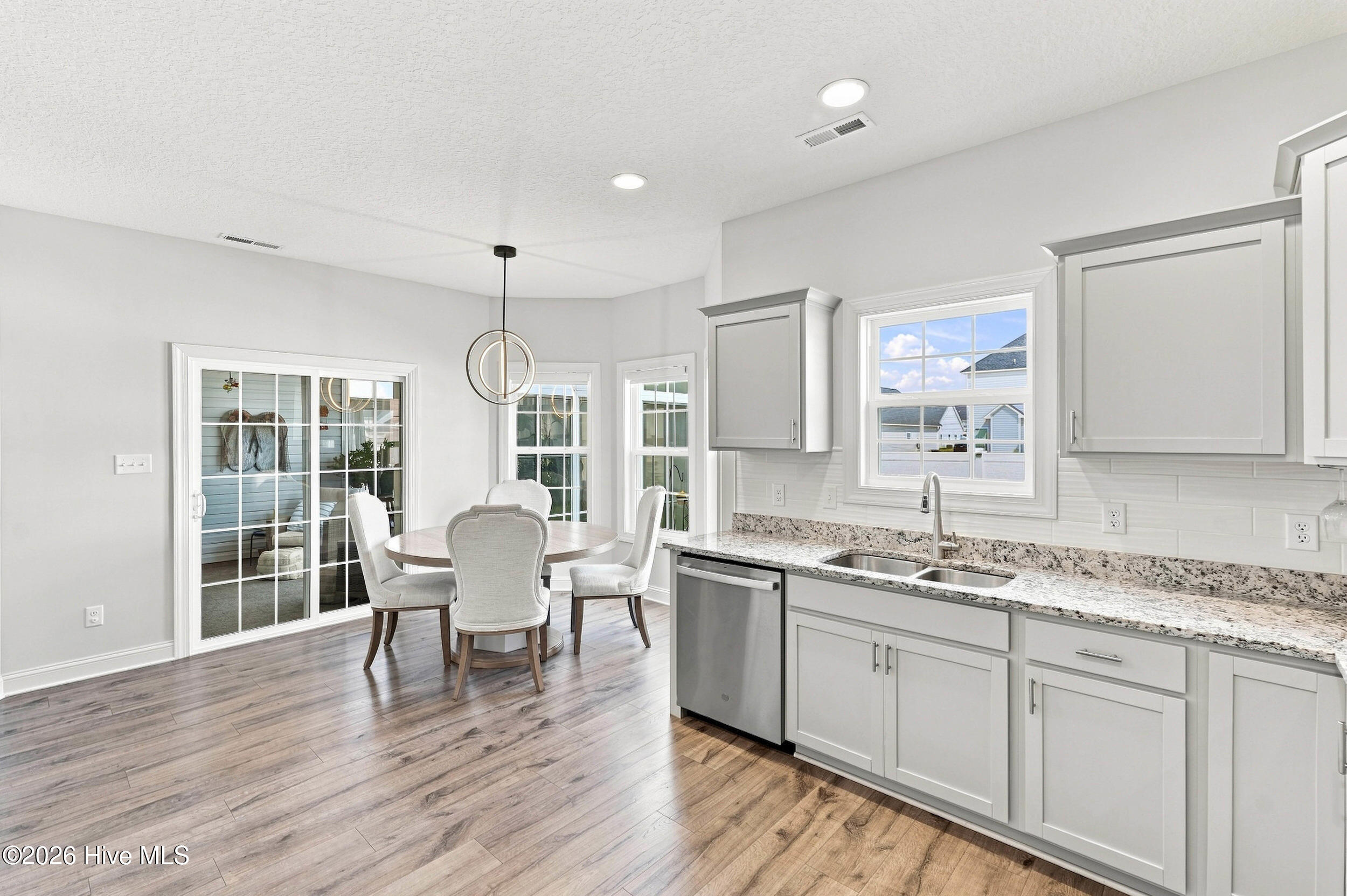 Bright kitchen with white cabinets and granite counters beside a dining table and sliding glass door.
