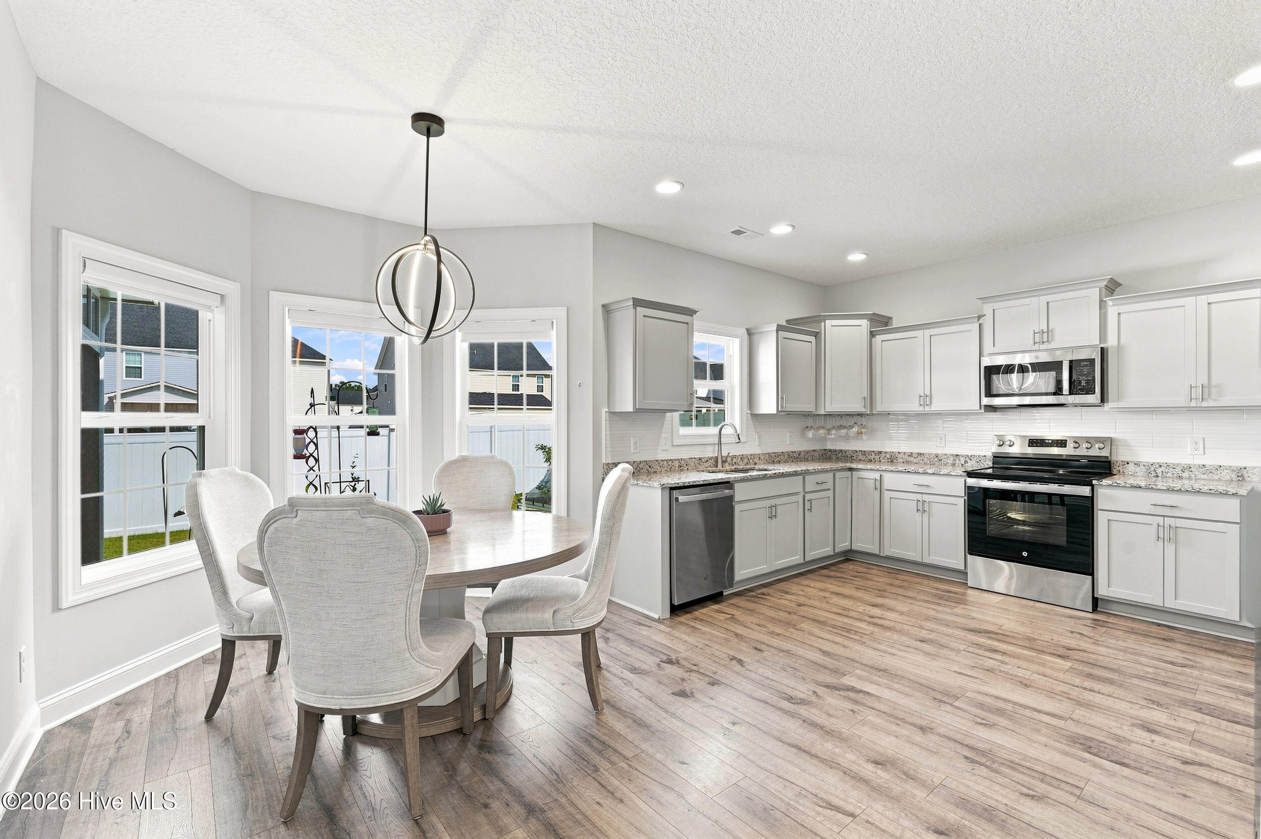 Open kitchen and dining area with white cabinets, stainless appliances, and a round table by large windows.