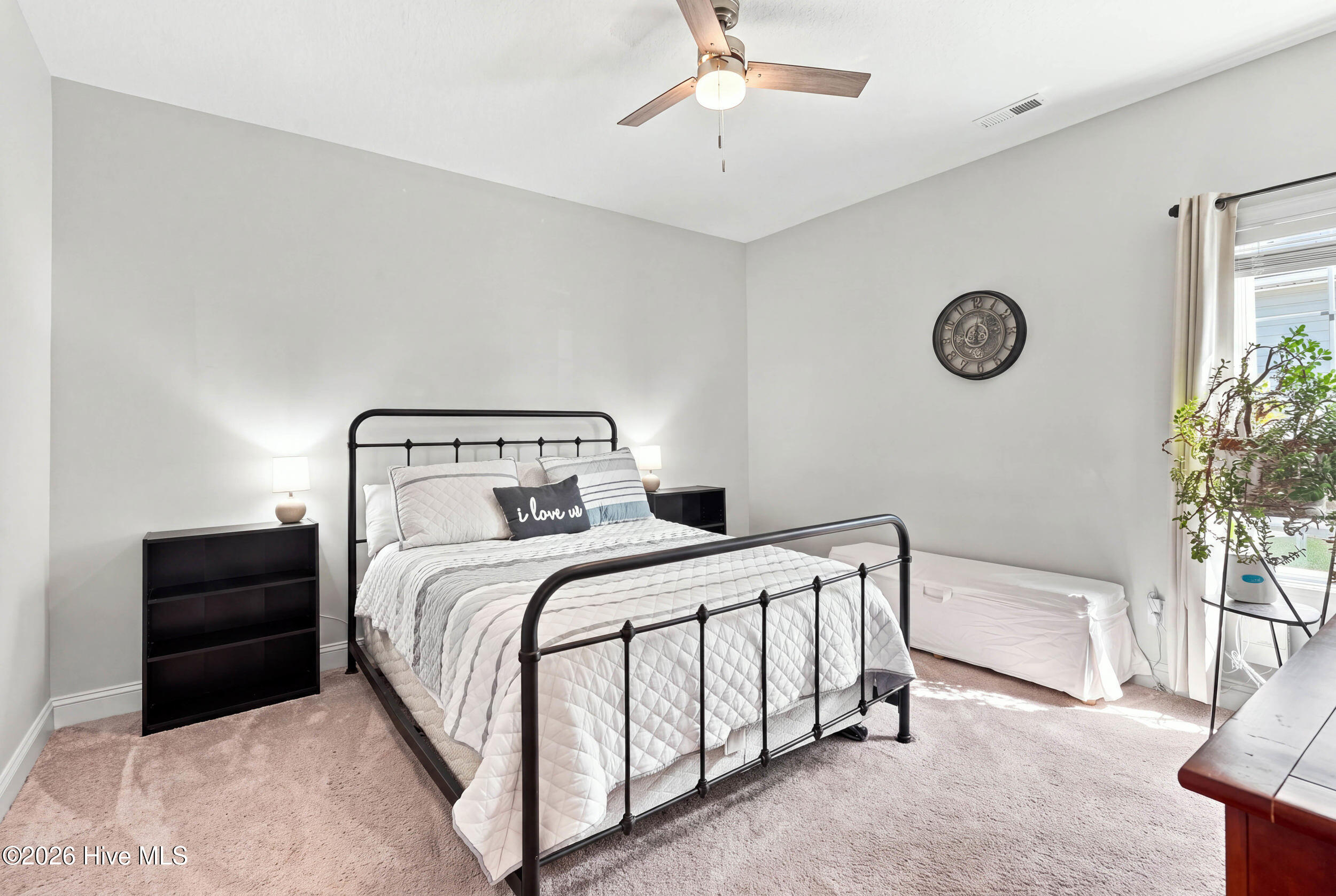 Bedroom with a black metal bed, white quilted bedding, and a sunlit window with a potted plant.