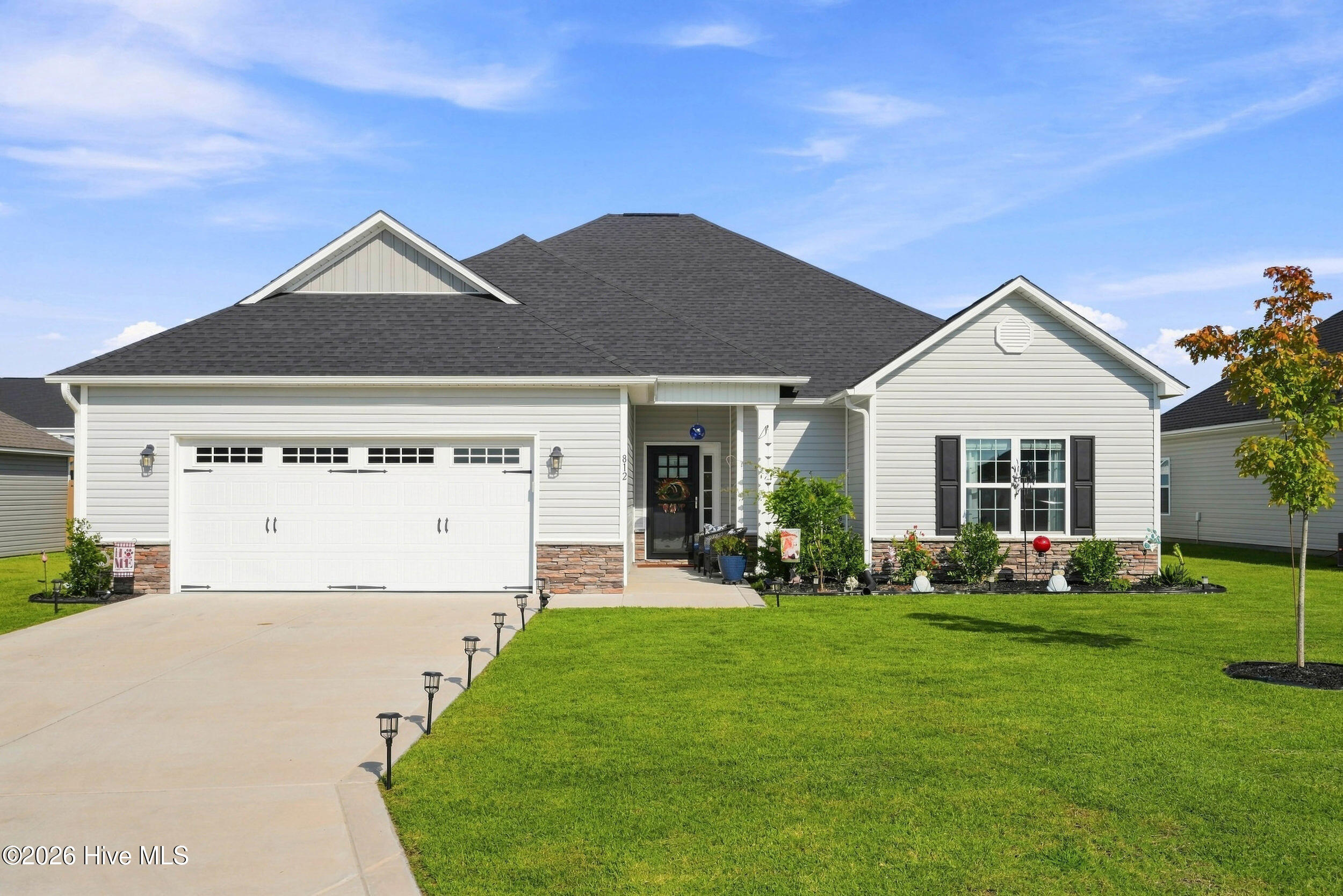 Single-story home with a two-car garage, stone accents, landscaped entry, and broad green lawn.