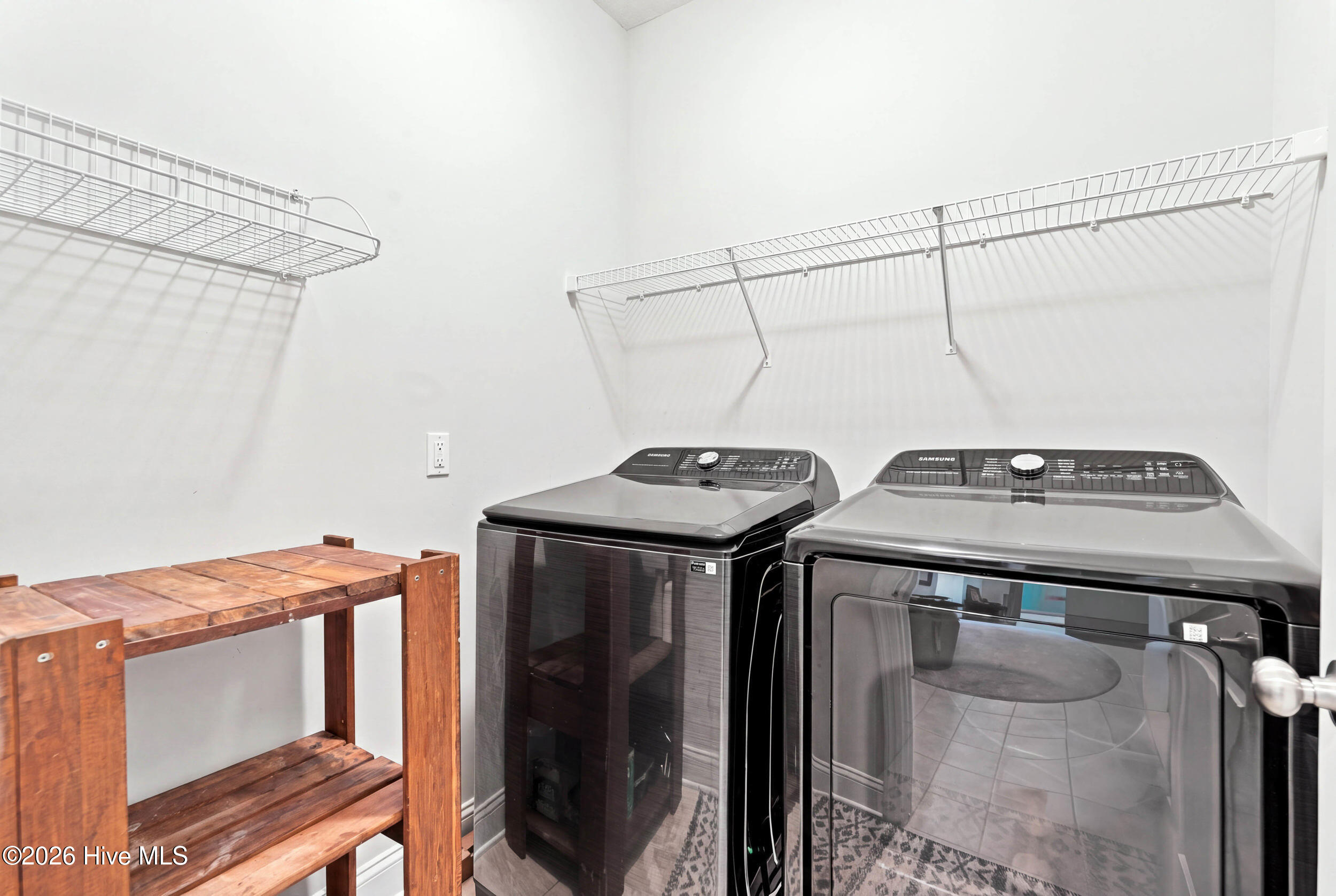 Laundry room with washer and dryer beneath wire shelves, beside a wooden shelving unit.