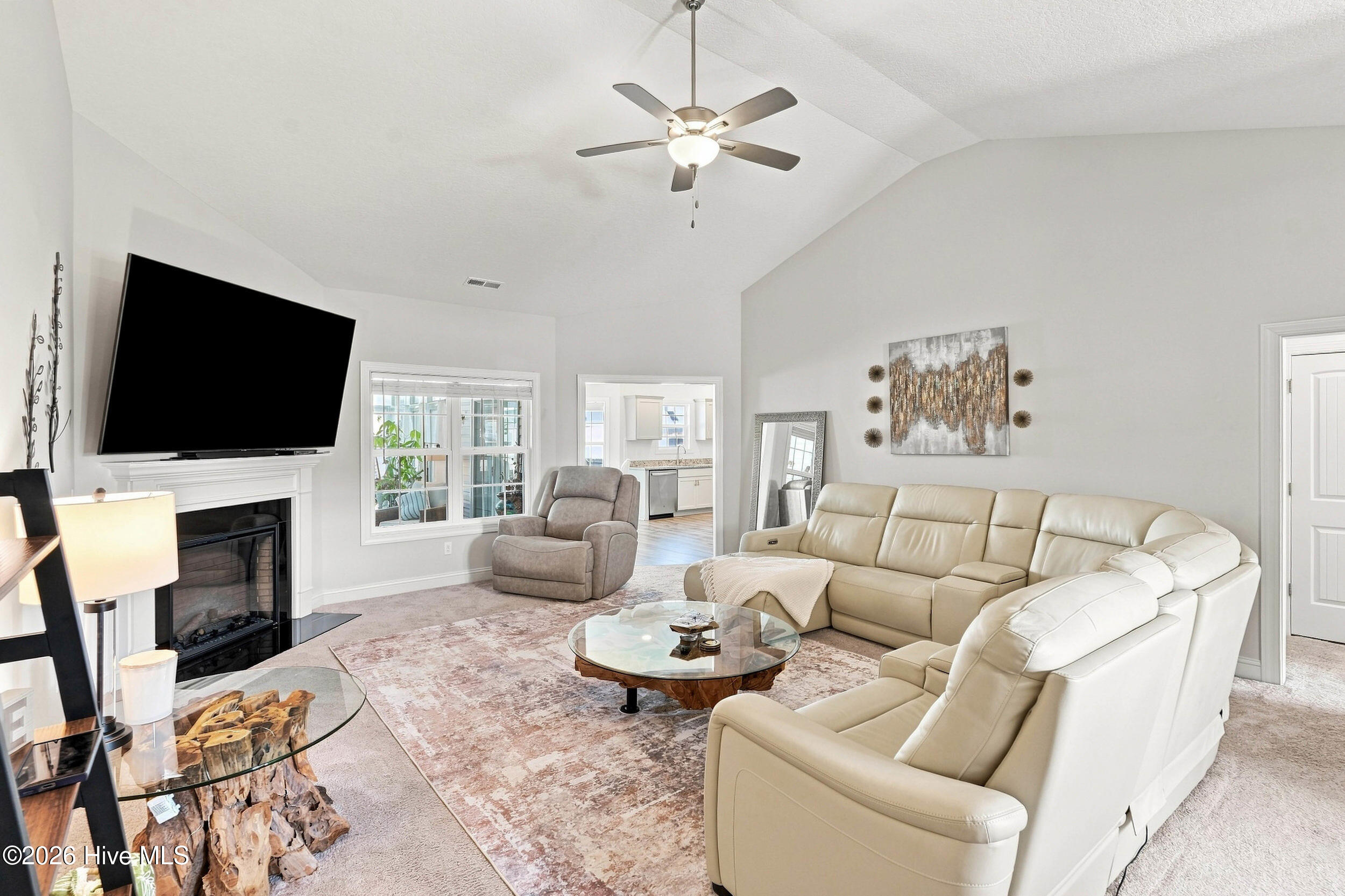 Furnished living room with a cream sectional, fireplace, mounted television, and vaulted ceiling.
