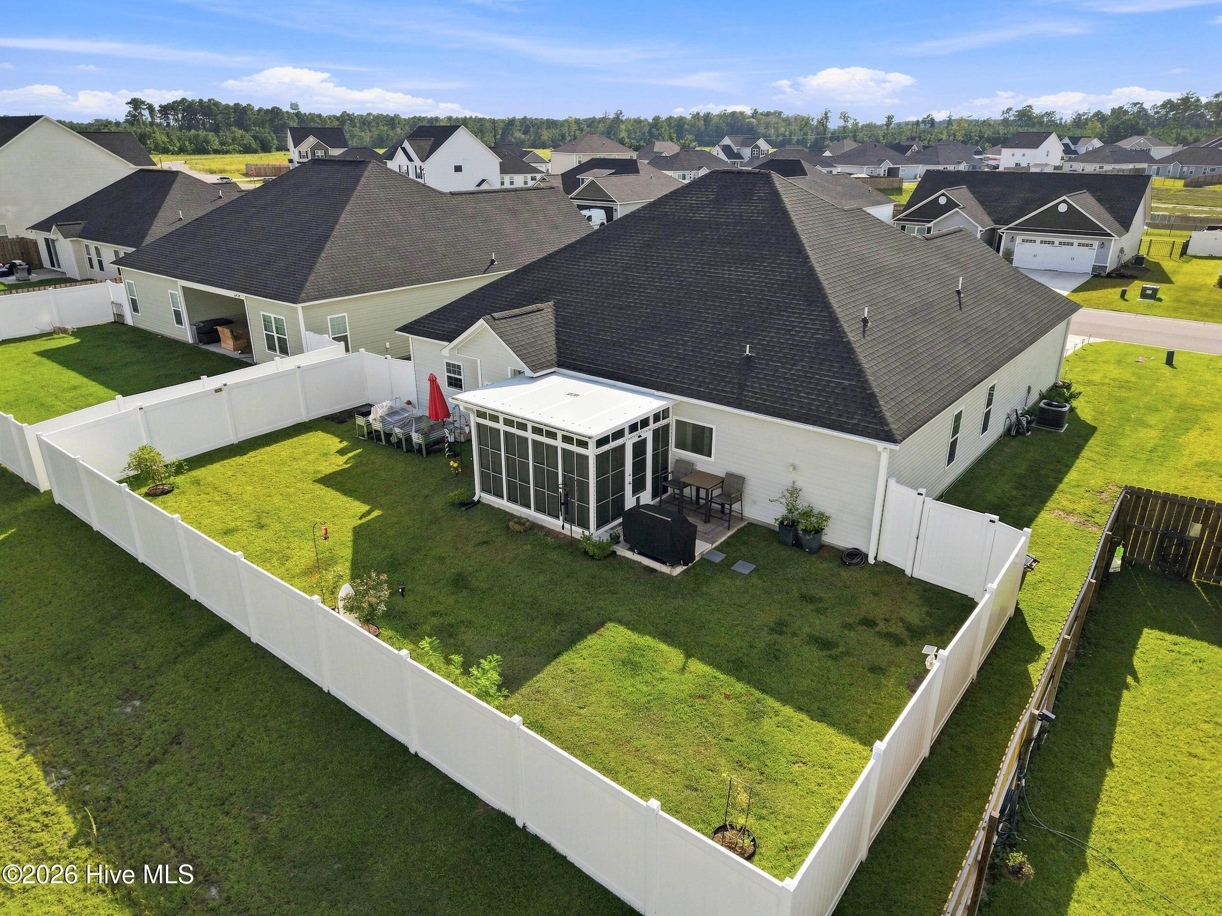 Aerial view of a fenced backyard with a screened porch and patio seating behind a light-colored home.