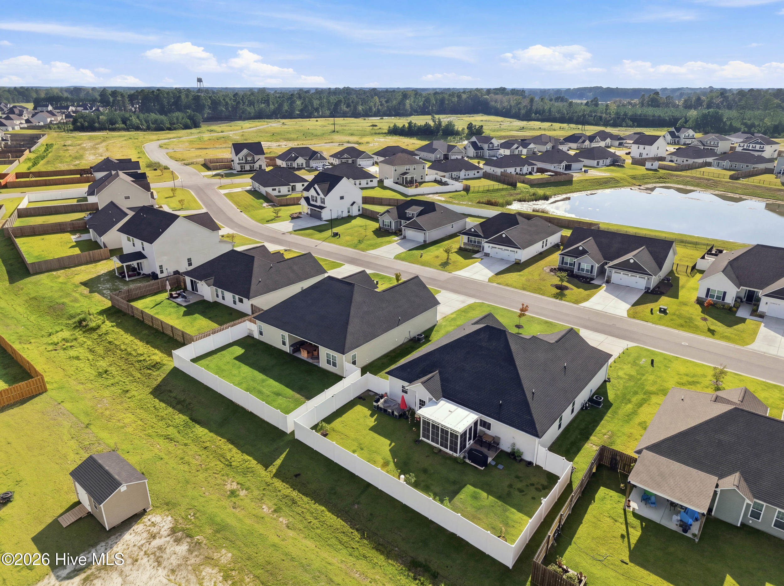 Aerial view of a home with a large fenced backyard and screened patio beside a neighborhood pond.