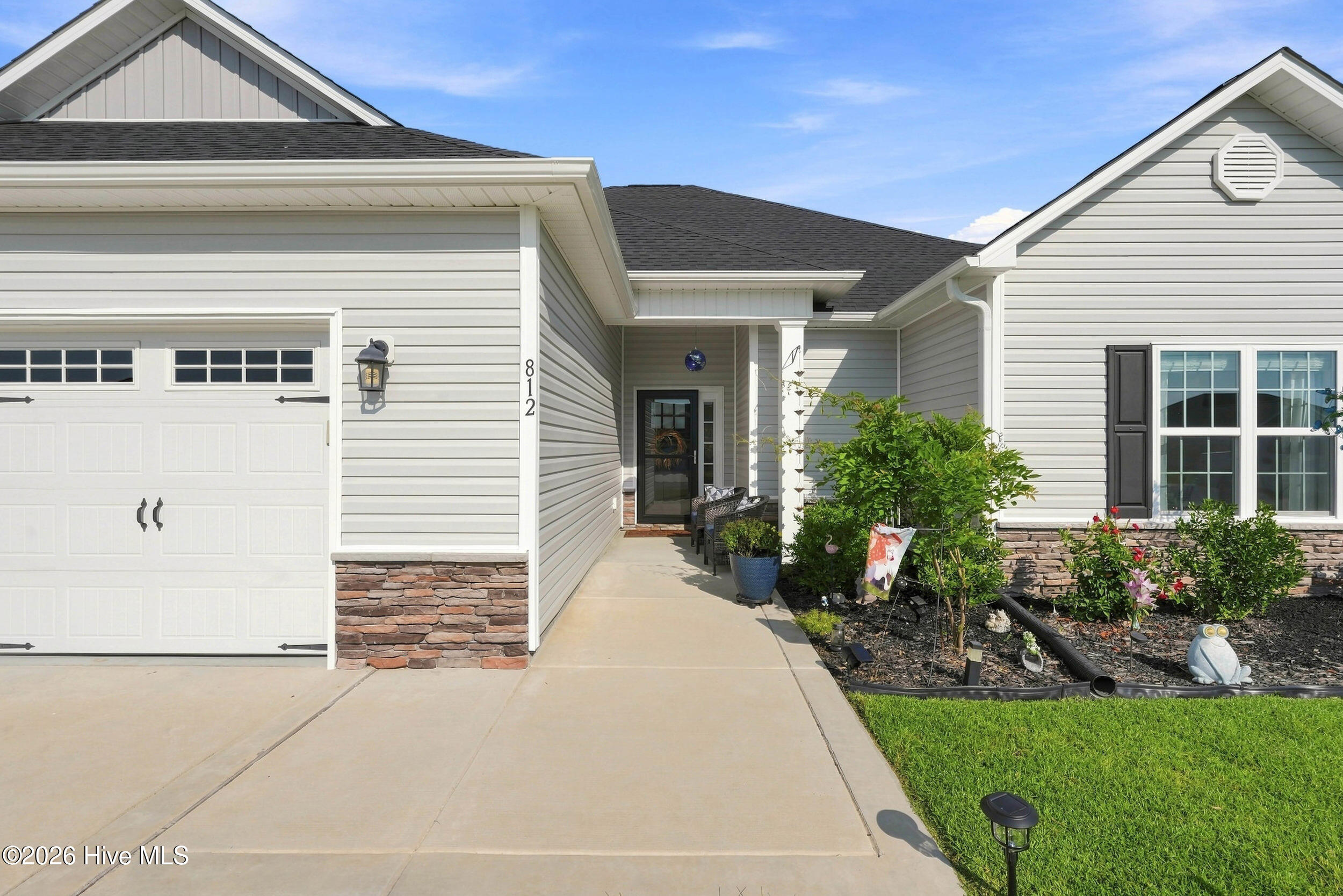 House exterior with a two-car garage, covered entry, stone accents, and landscaped garden.