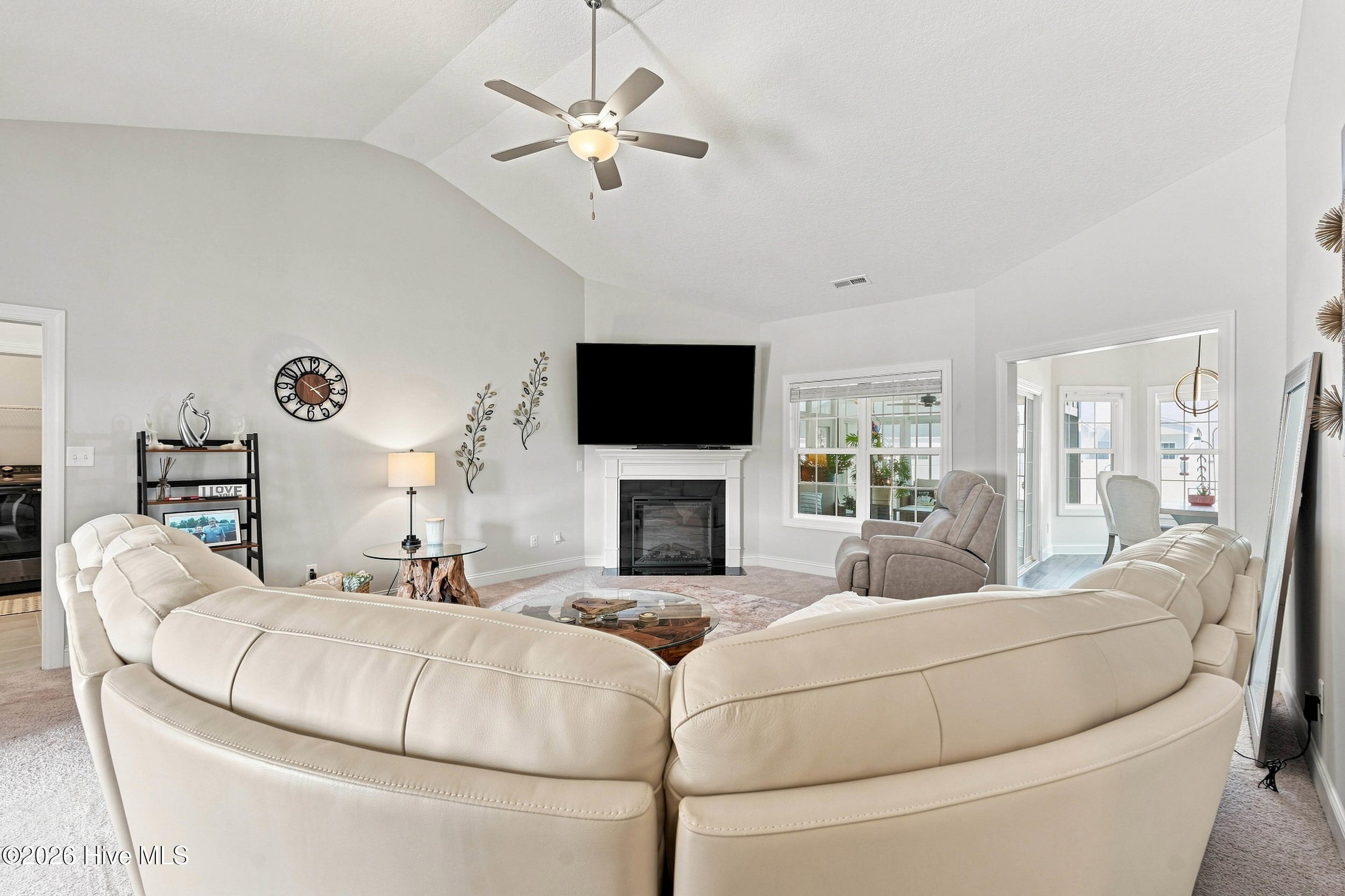 Furnished living room with a vaulted ceiling, white sectional, fireplace, and television.