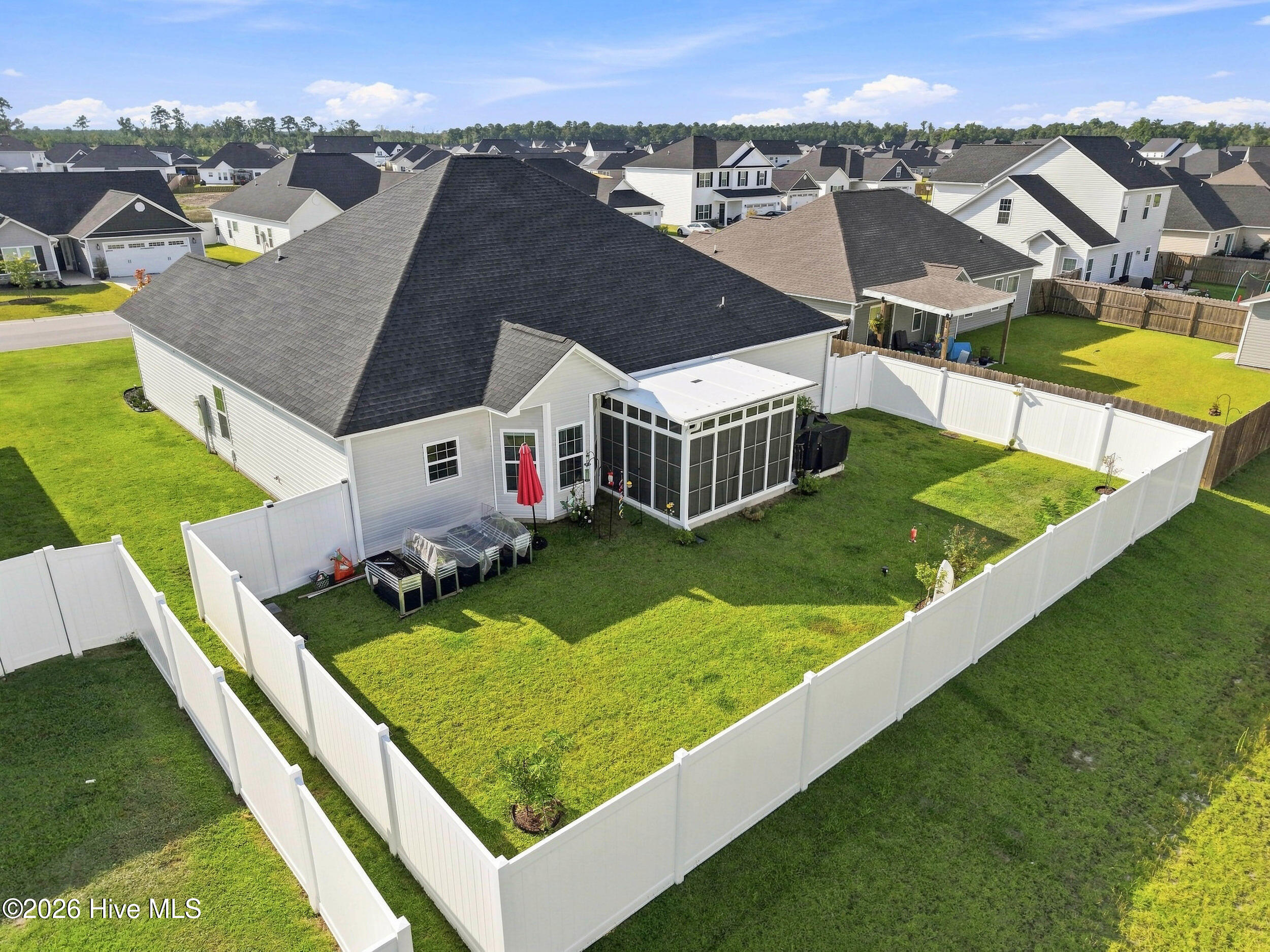 Aerial view of a fenced backyard with a screened porch and neighboring homes beyond.