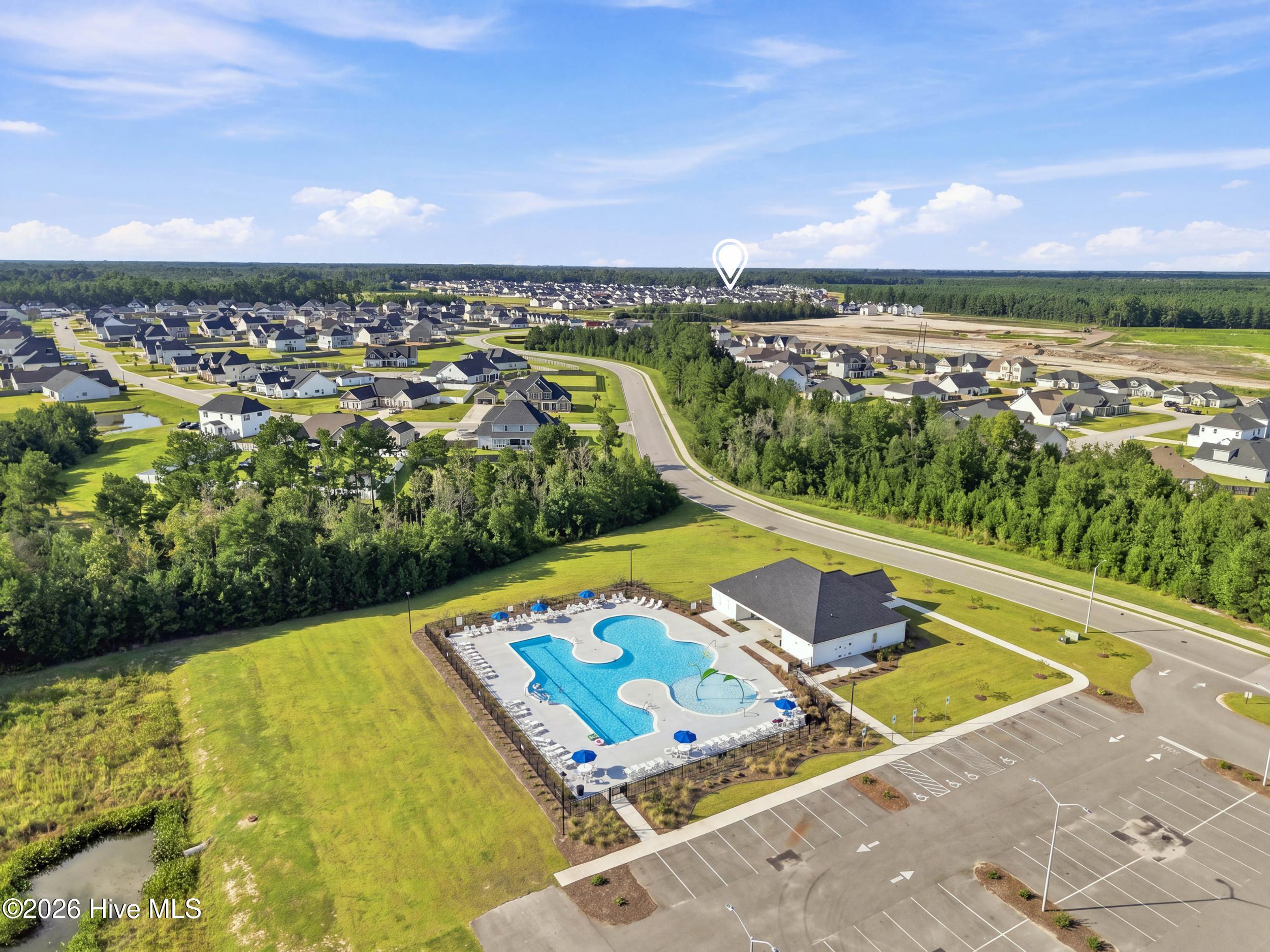 Aerial view of a neighborhood pool and amenity building surrounded by homes and trees.