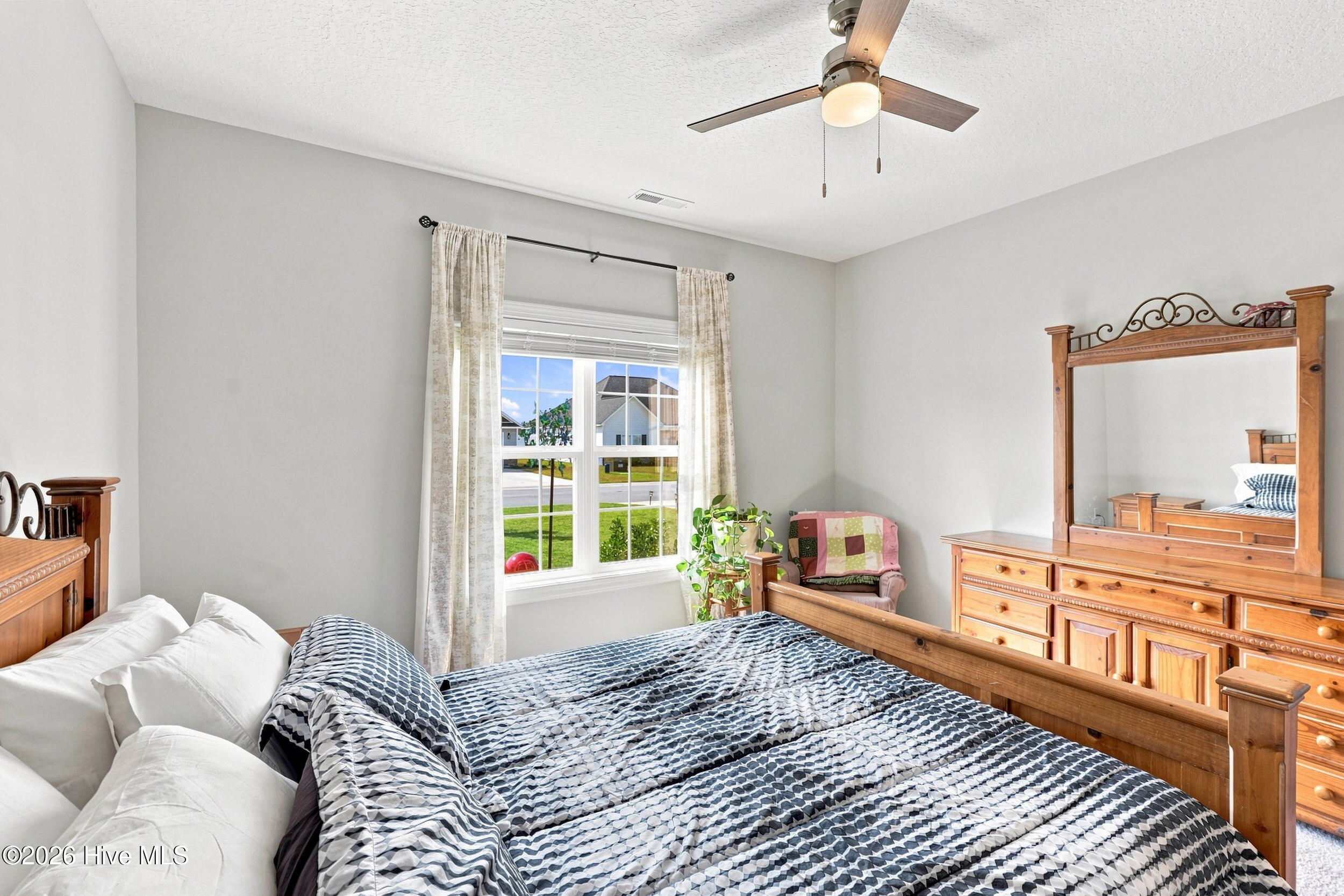 Bedroom with a wooden four-poster bed, patterned bedding, matching dresser, and a bright window.