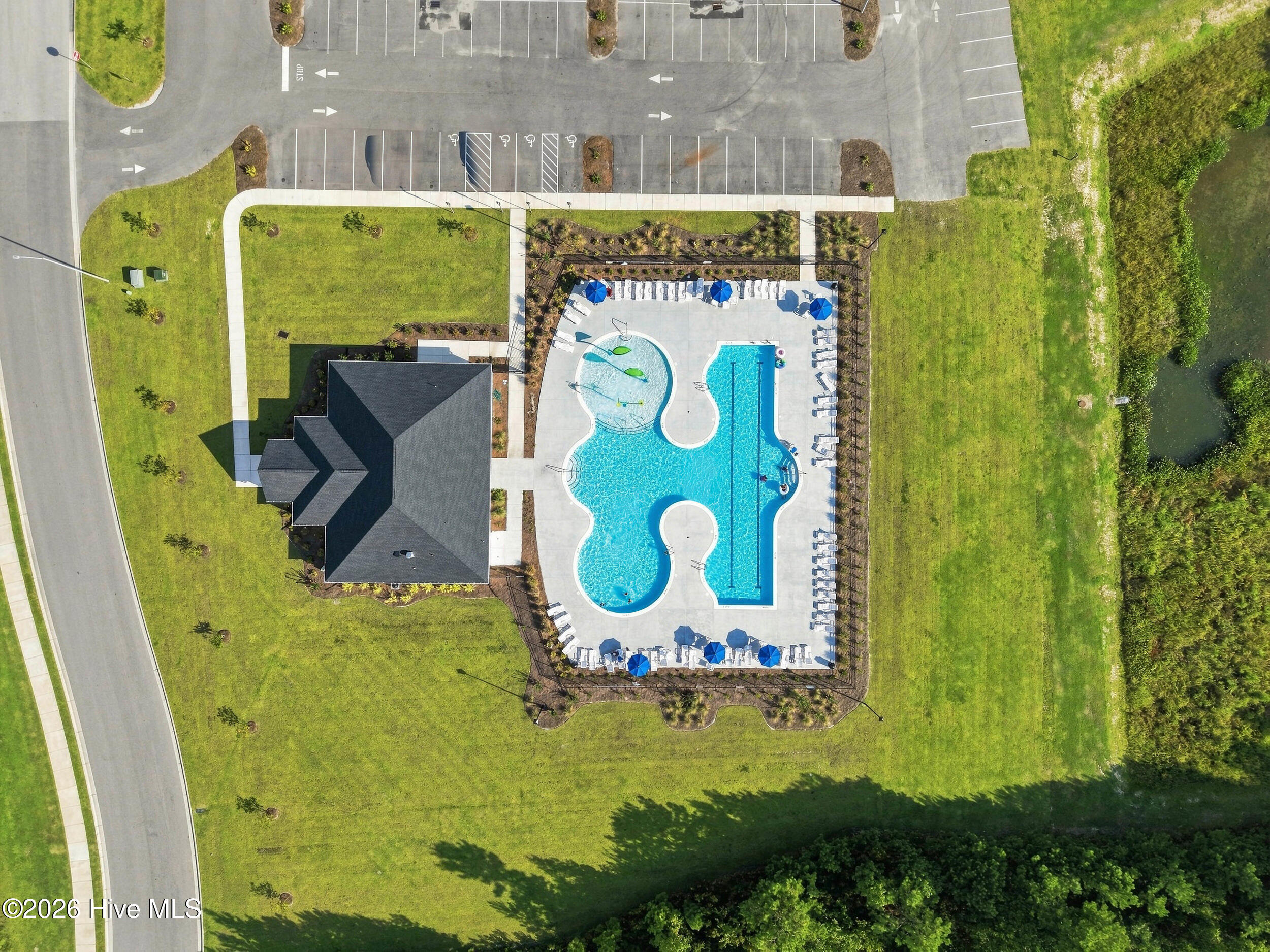 Aerial view of a landscaped property with two outdoor pools, blue umbrellas, and a nearby building.