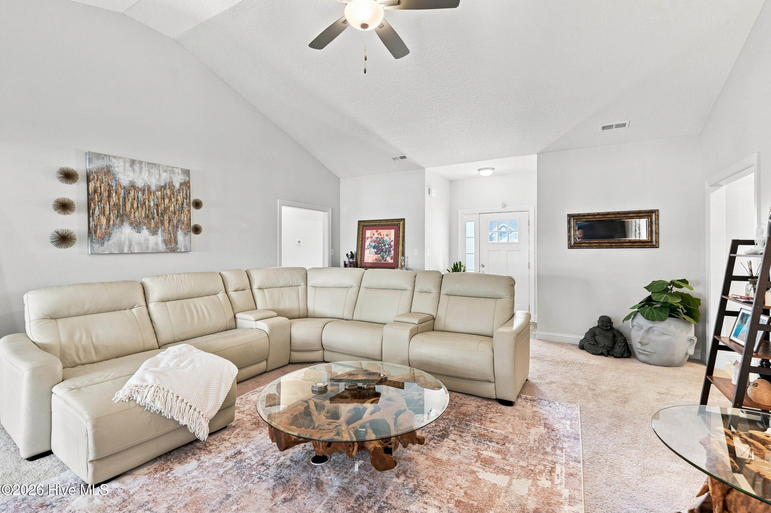 Living room with a cream sectional, glass coffee table, patterned rug, and vaulted ceiling.