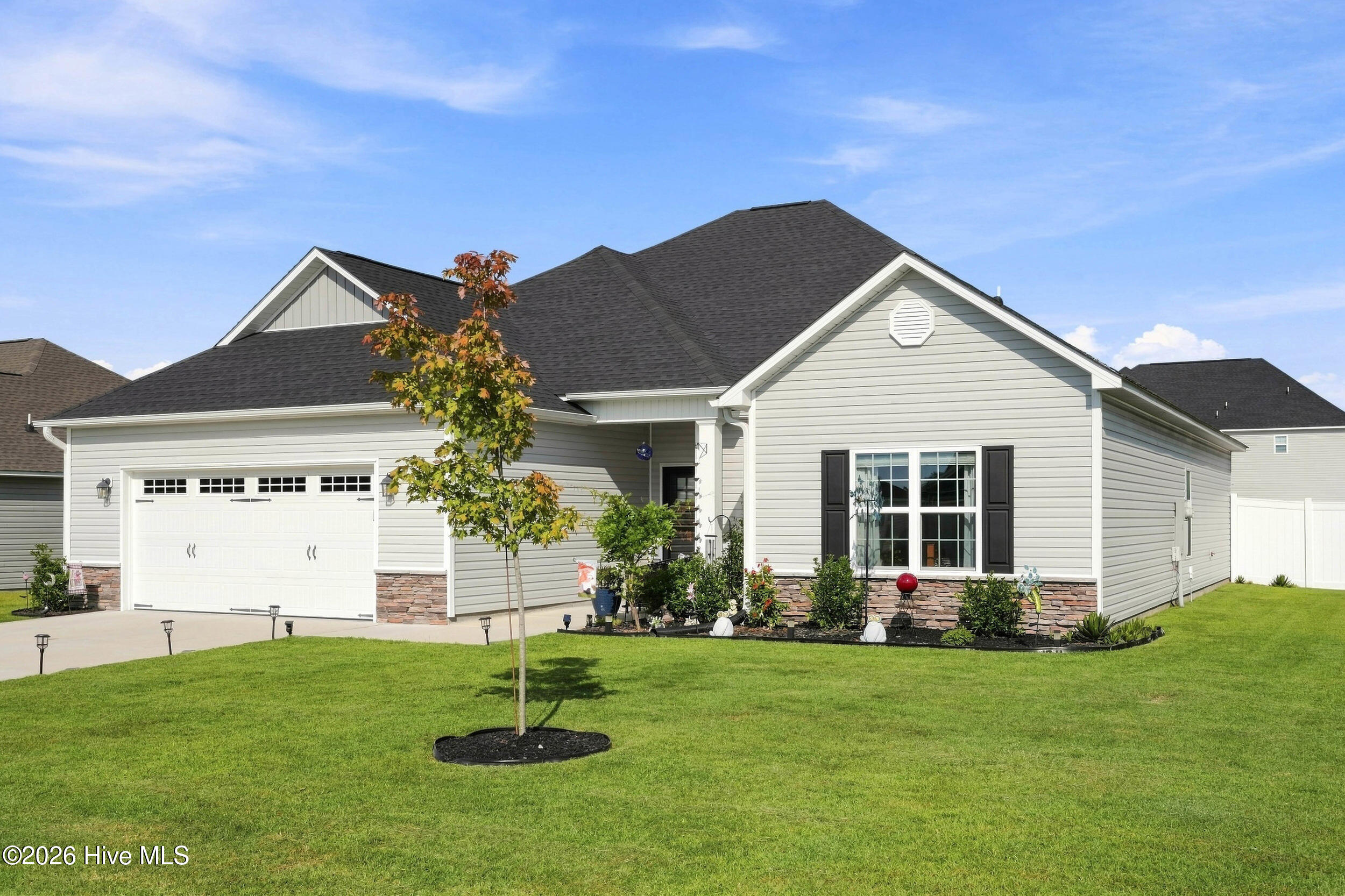Light gray house with attached two-car garage, stone accents, landscaped beds, and a wide green lawn.