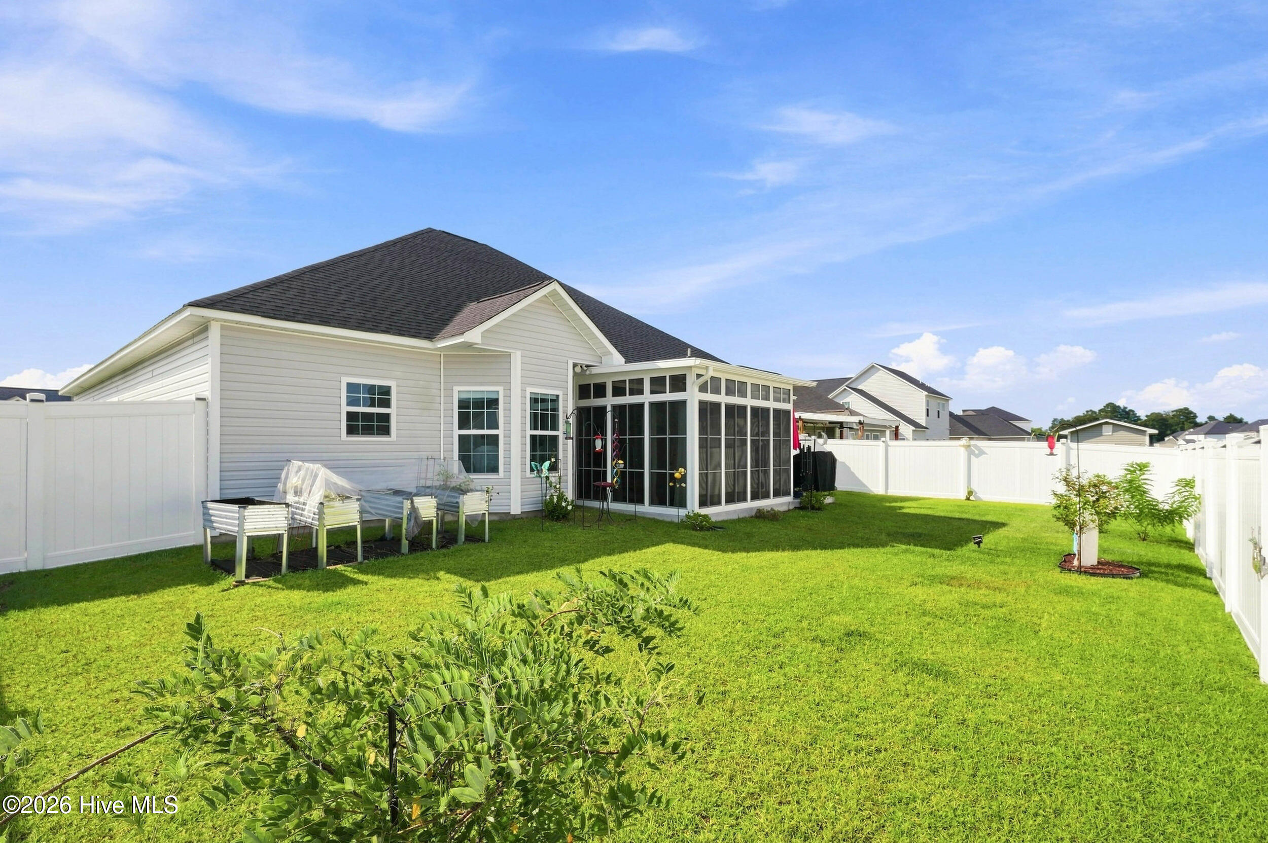 House backyard with a glass-enclosed sunroom, white privacy fence, raised garden beds, and green lawn.
