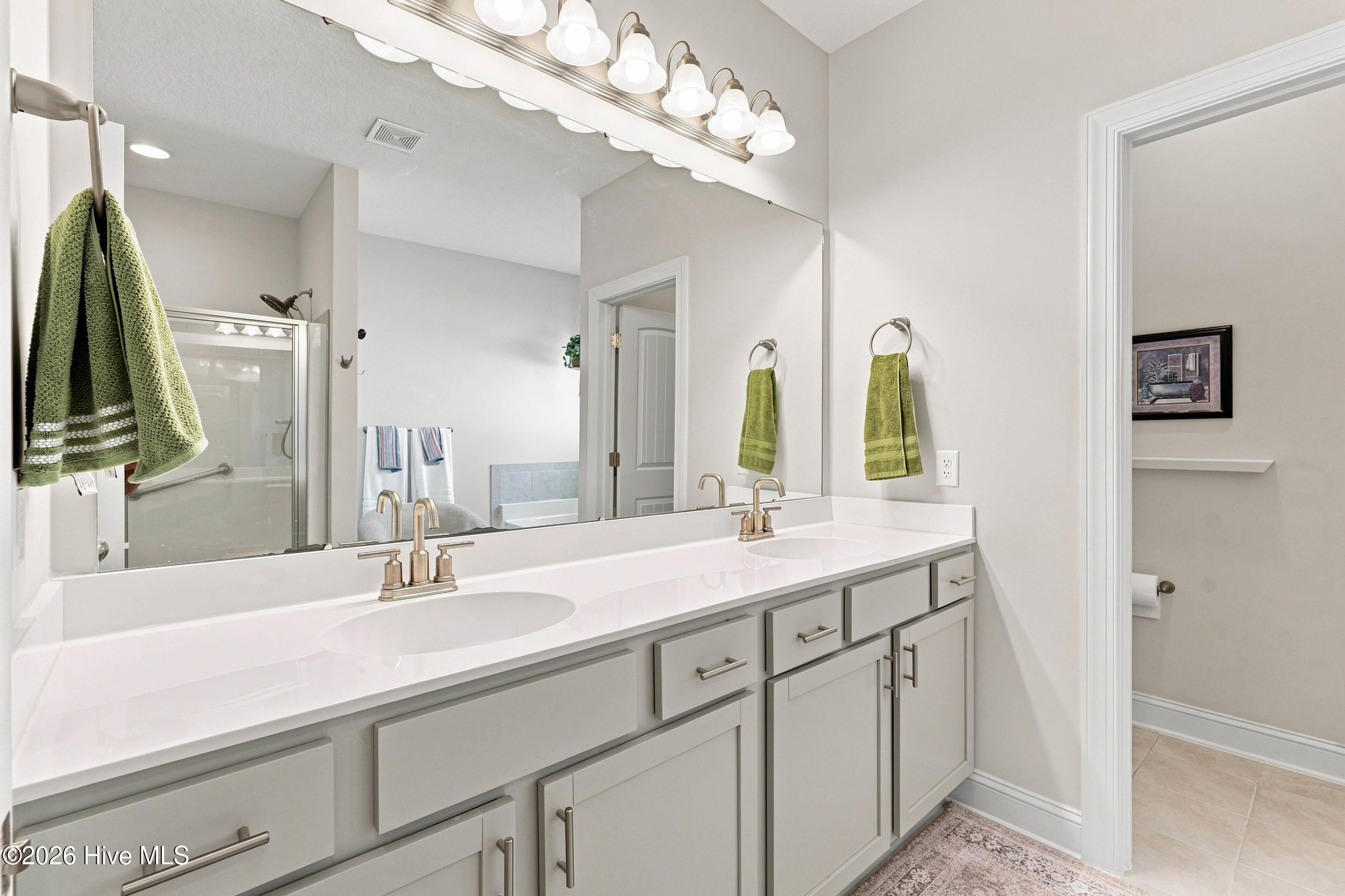 Bathroom with a double-sink vanity, gray cabinets, large mirrors, and a glass-enclosed shower.