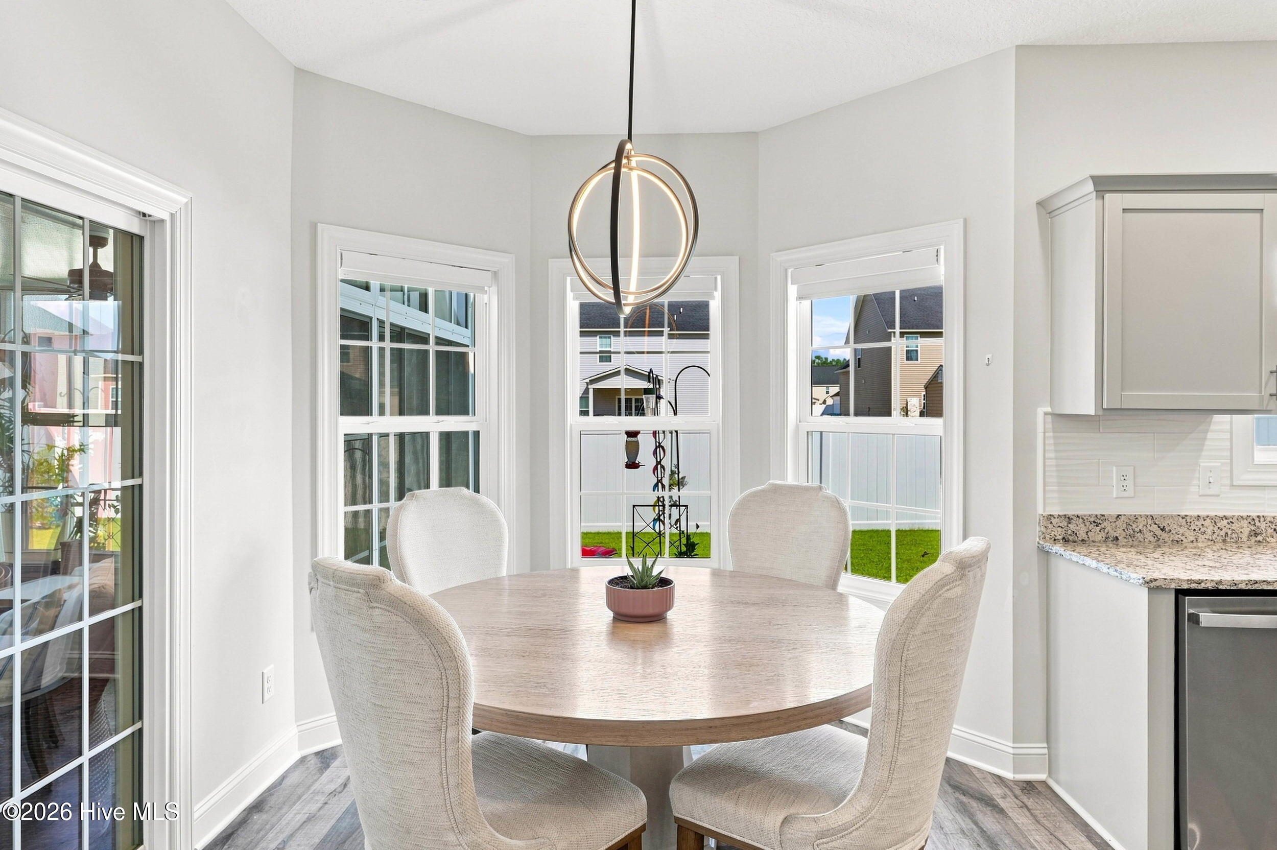 Dining nook with a round table, upholstered chairs, spherical pendant light, and large windows.