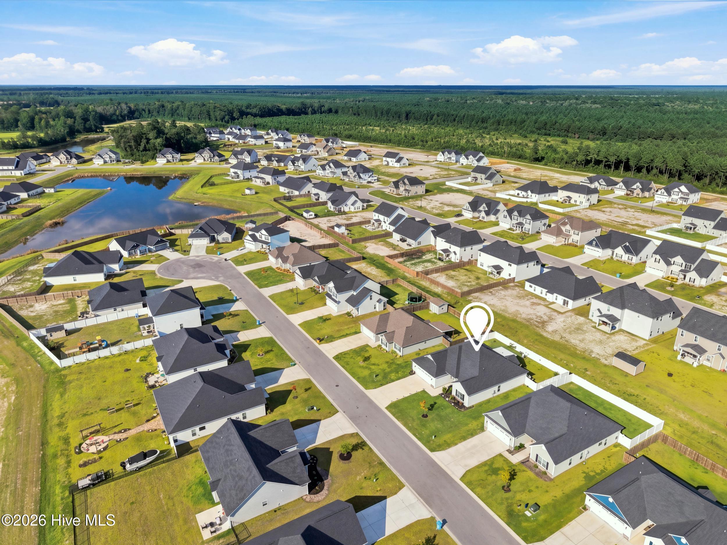 Aerial view of the marked home in a neighborhood with a pond and surrounding woods.