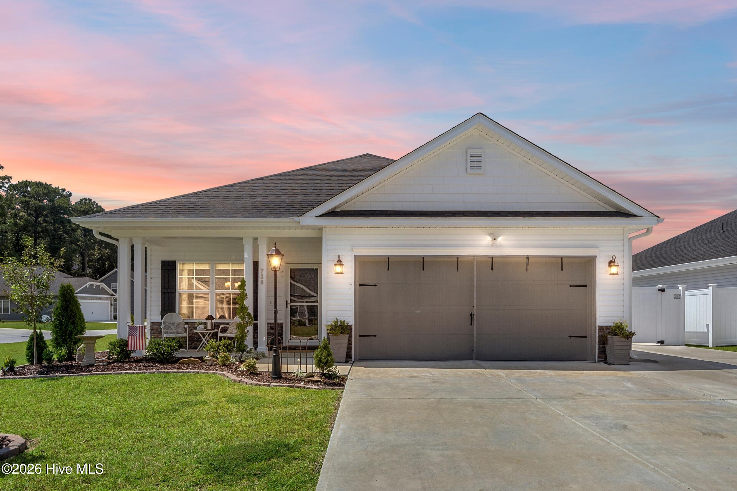 White house with a double garage and covered porch beneath a pink sunset sky.