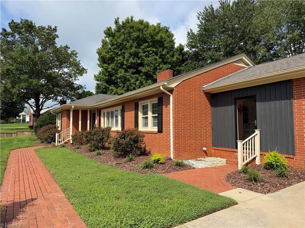 Red brick building with dark entrance siding, black shutters, and a curved brick walkway across the lawn.