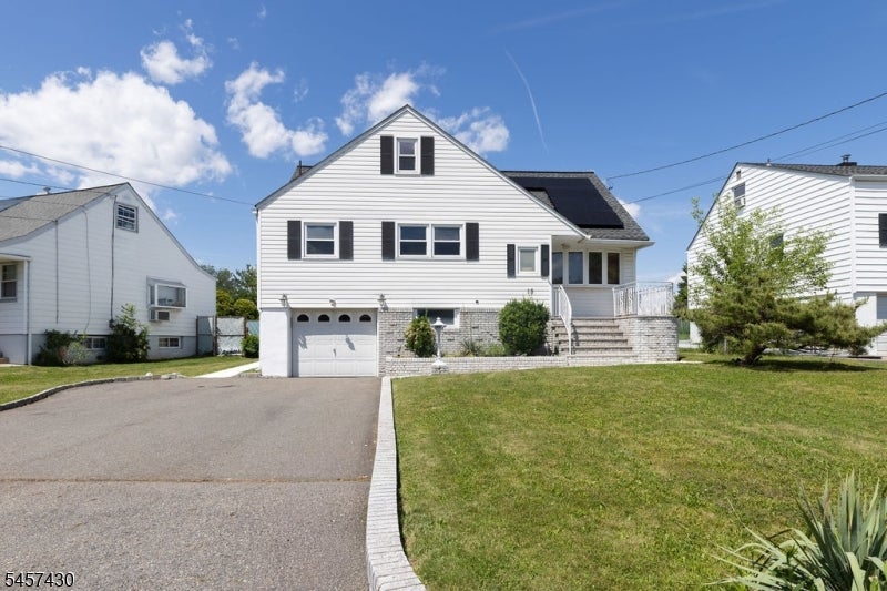 White two-story house with black shutters, an attached garage, solar panels, and a broad driveway.