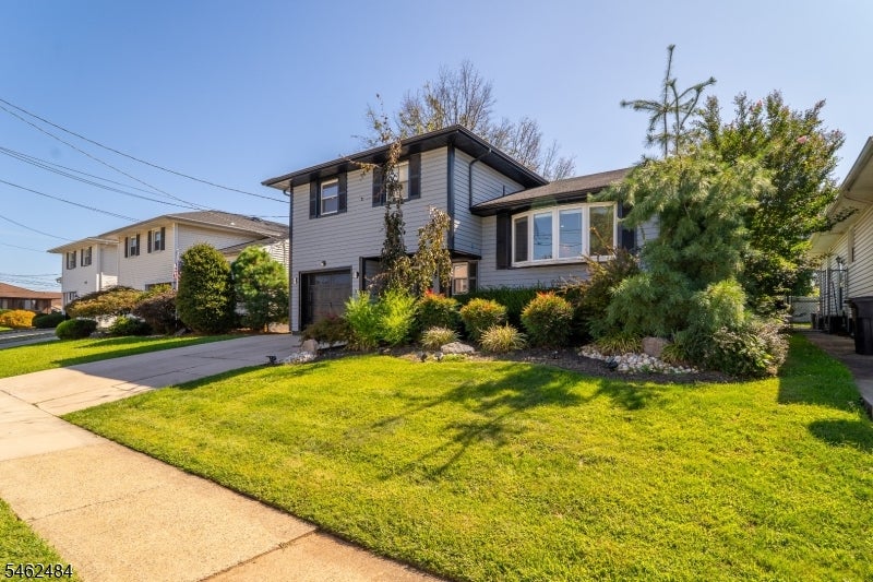 Two-story gray house with a dark garage, landscaped shrubs, driveway, and broad green front lawn.