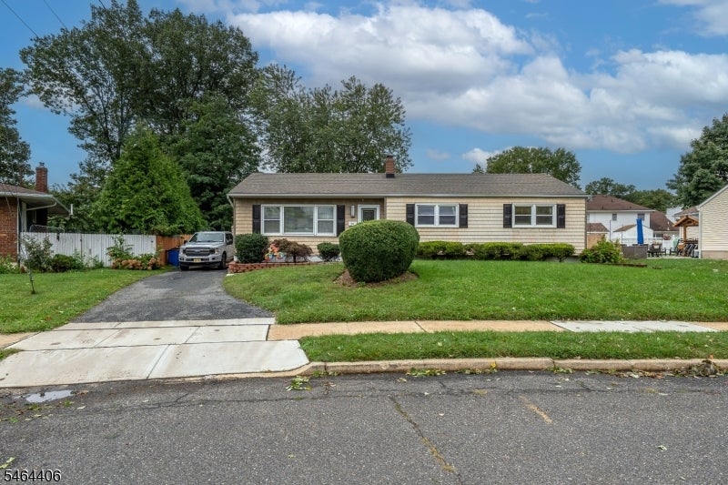 Single-story beige ranch house with black shutters, a front lawn, and a driveway.