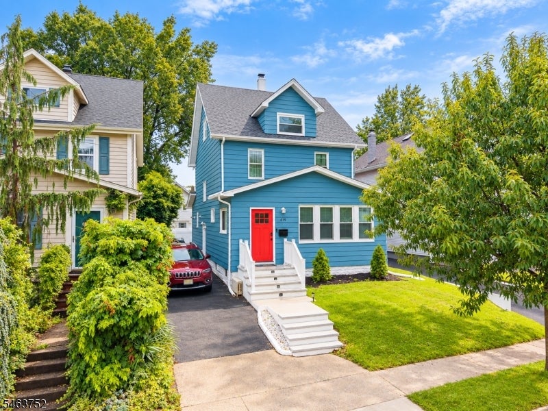 Blue two-story house with a red front door, white steps, and a small front lawn.