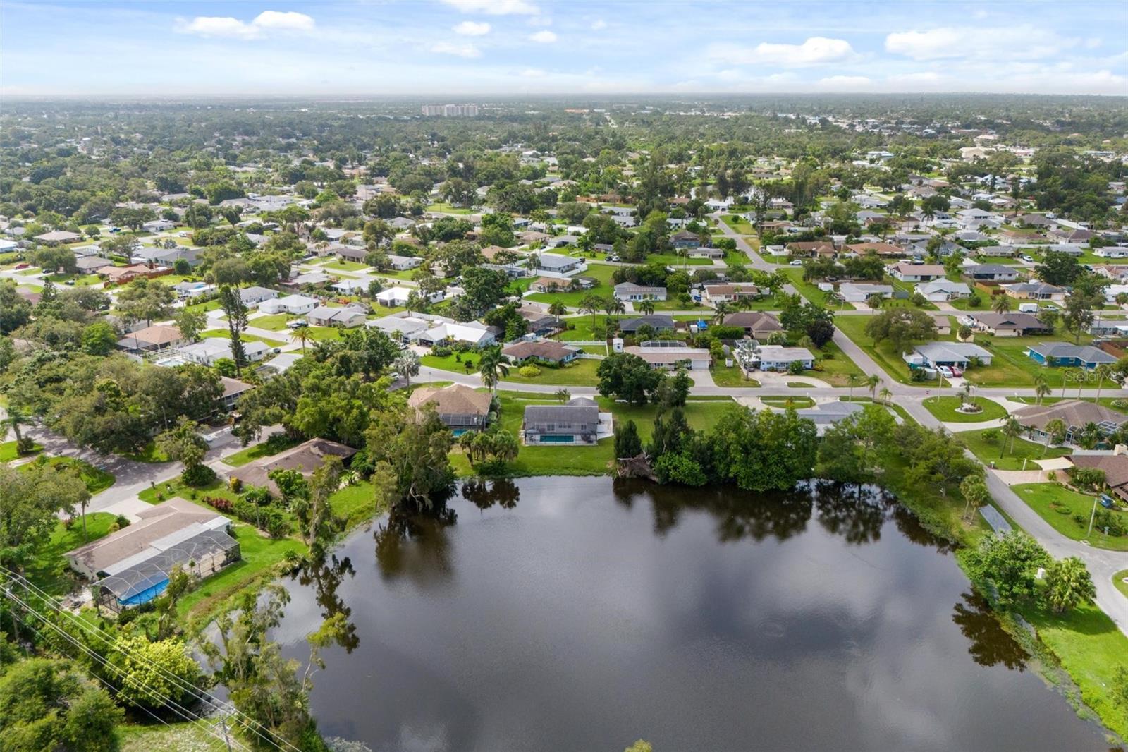 Aerial view of a residential neighborhood and pond, with homes and tree-lined streets stretching into the distance.