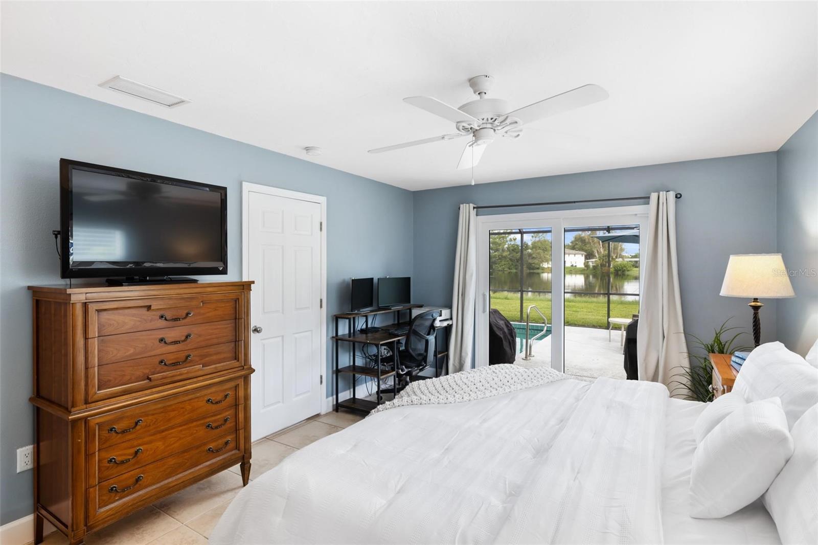 Bedroom with a white bed and sliding glass doors overlooking a pool and pond.