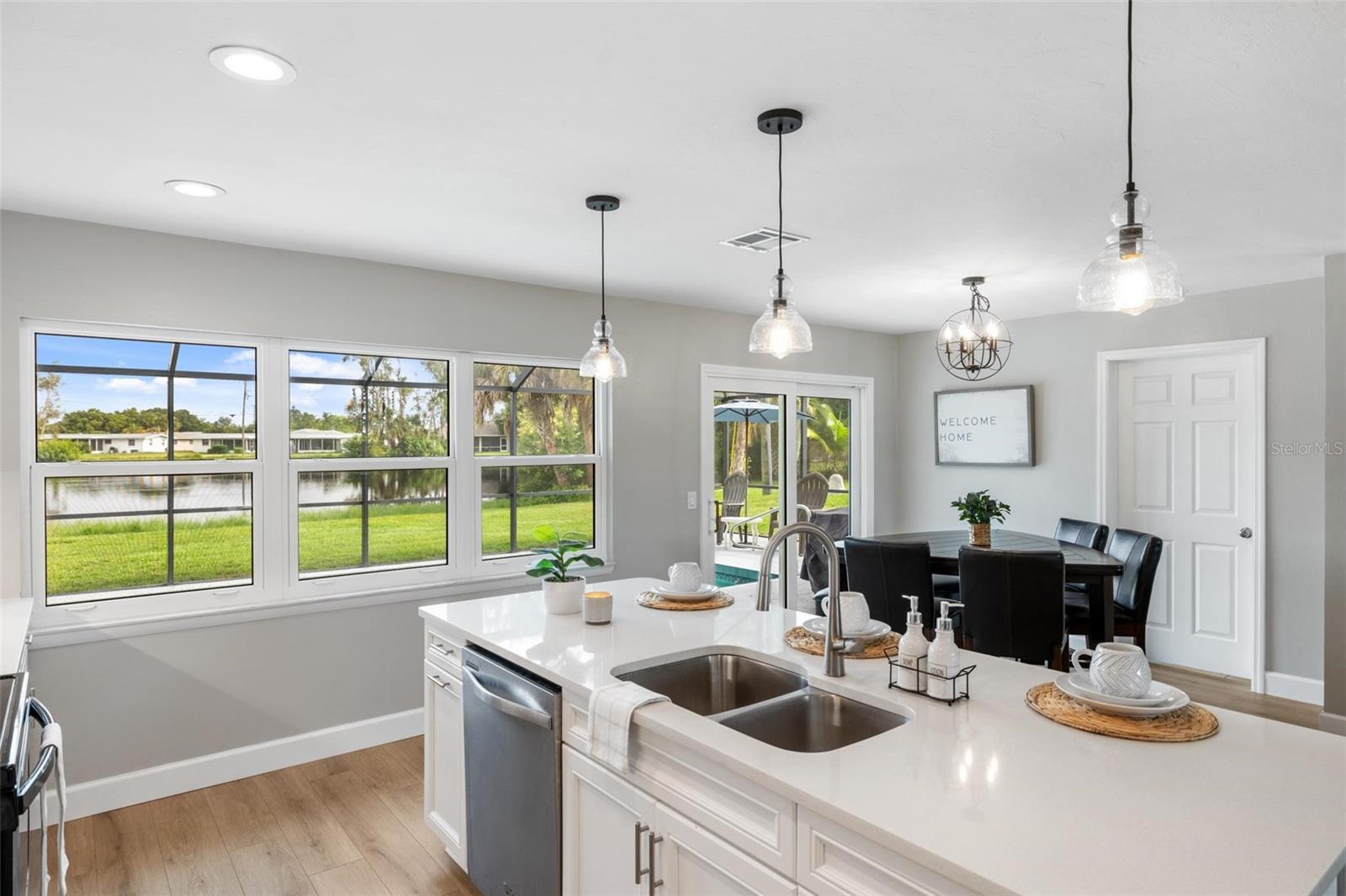 Bright kitchen with a large white island and dining area beside windows overlooking a canal.