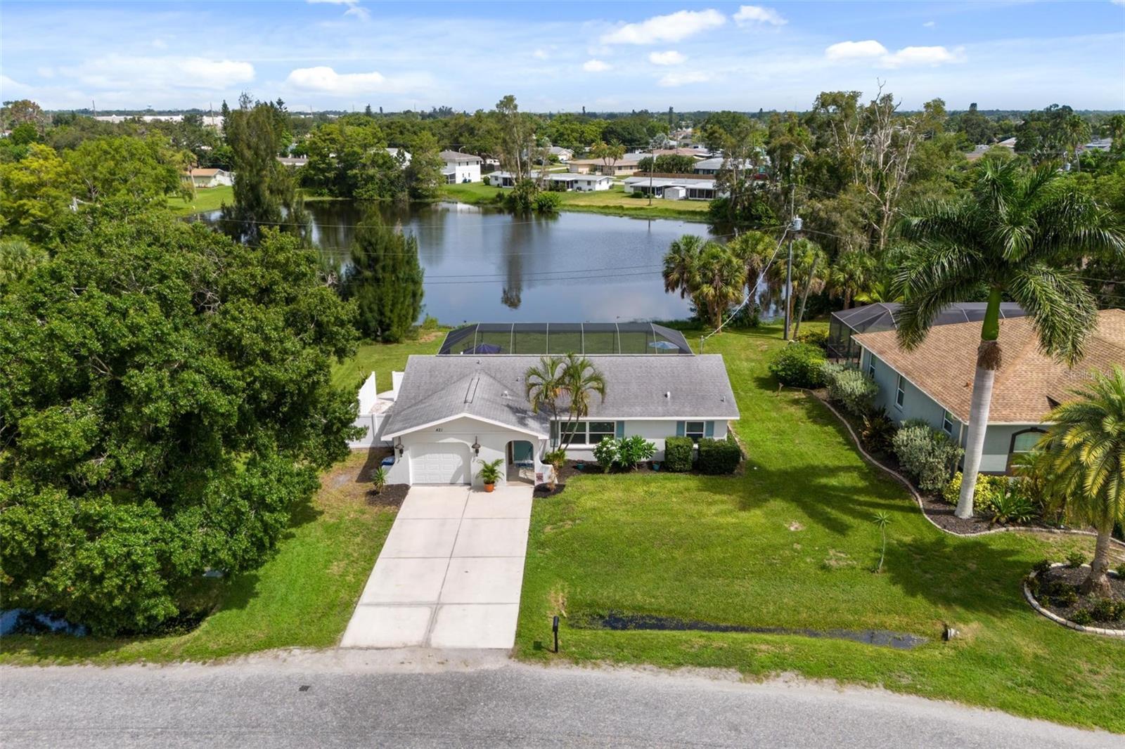 Aerial view of a home beside a lake, with its driveway and screened backyard visible.